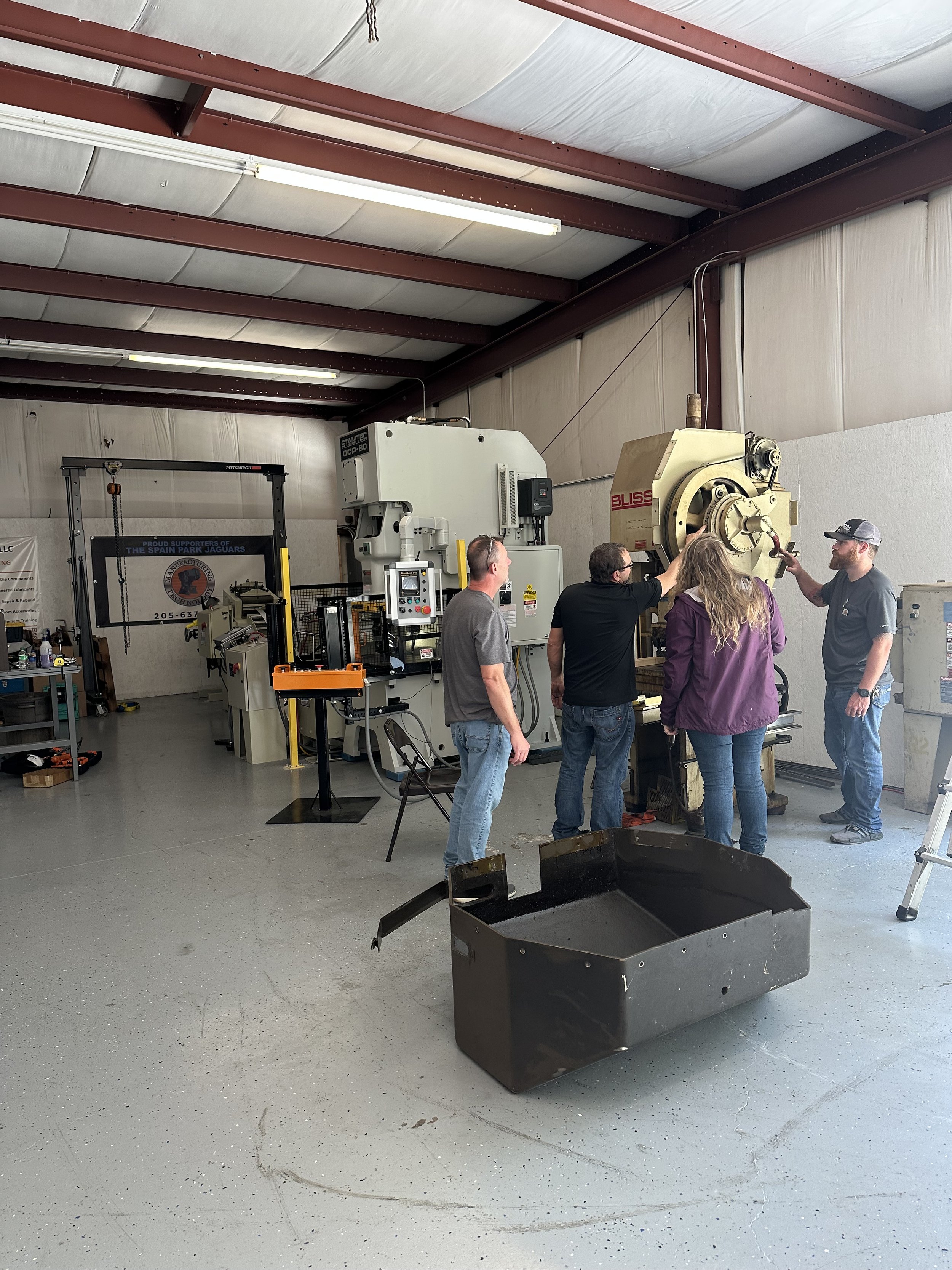 Five people working together in a machine shop, examining a large industrial machine, with various tools and equipment around.