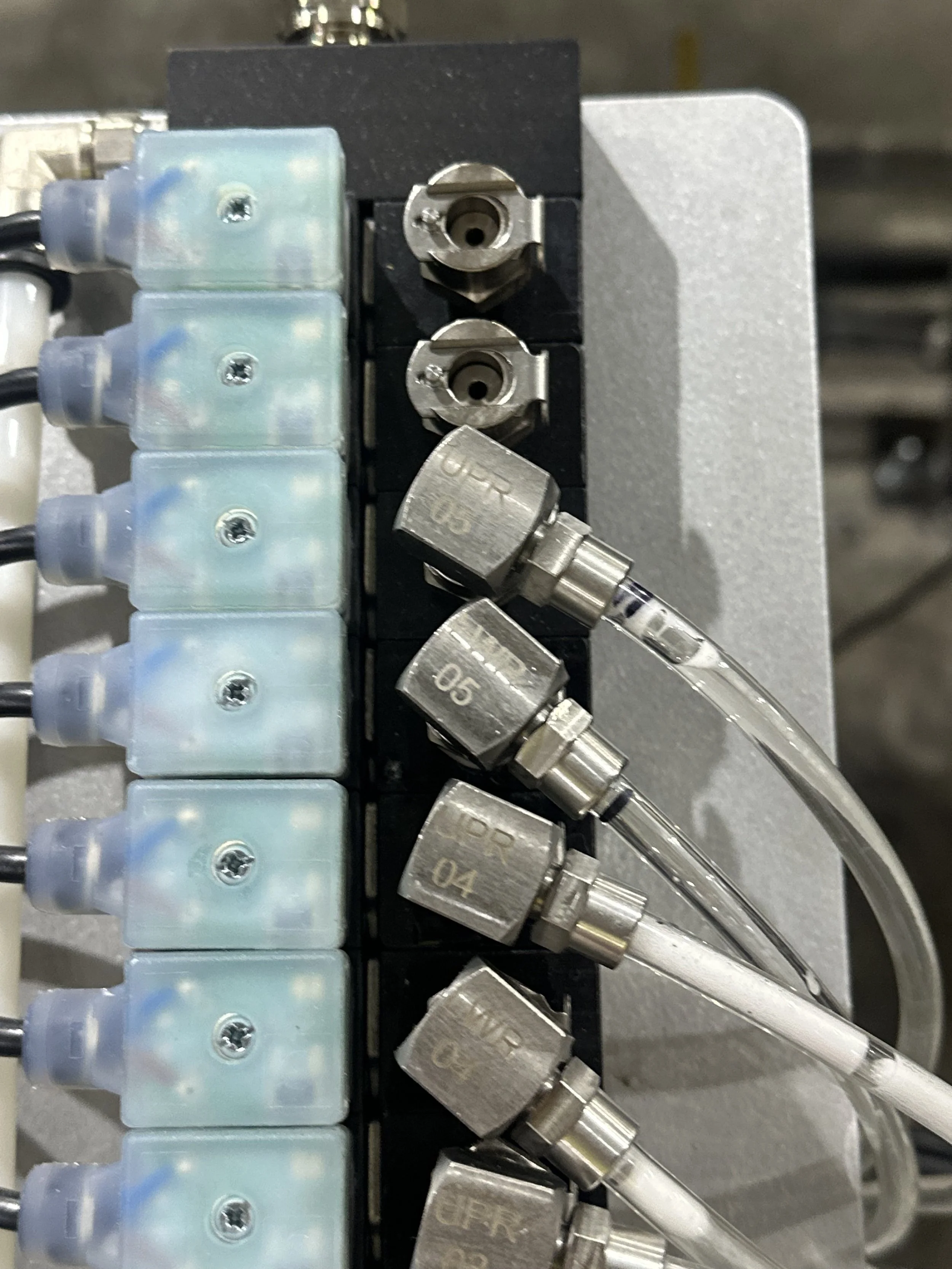 Close-up of a metallic industrial valve manifold with multiple hoses and fittings connected to it.