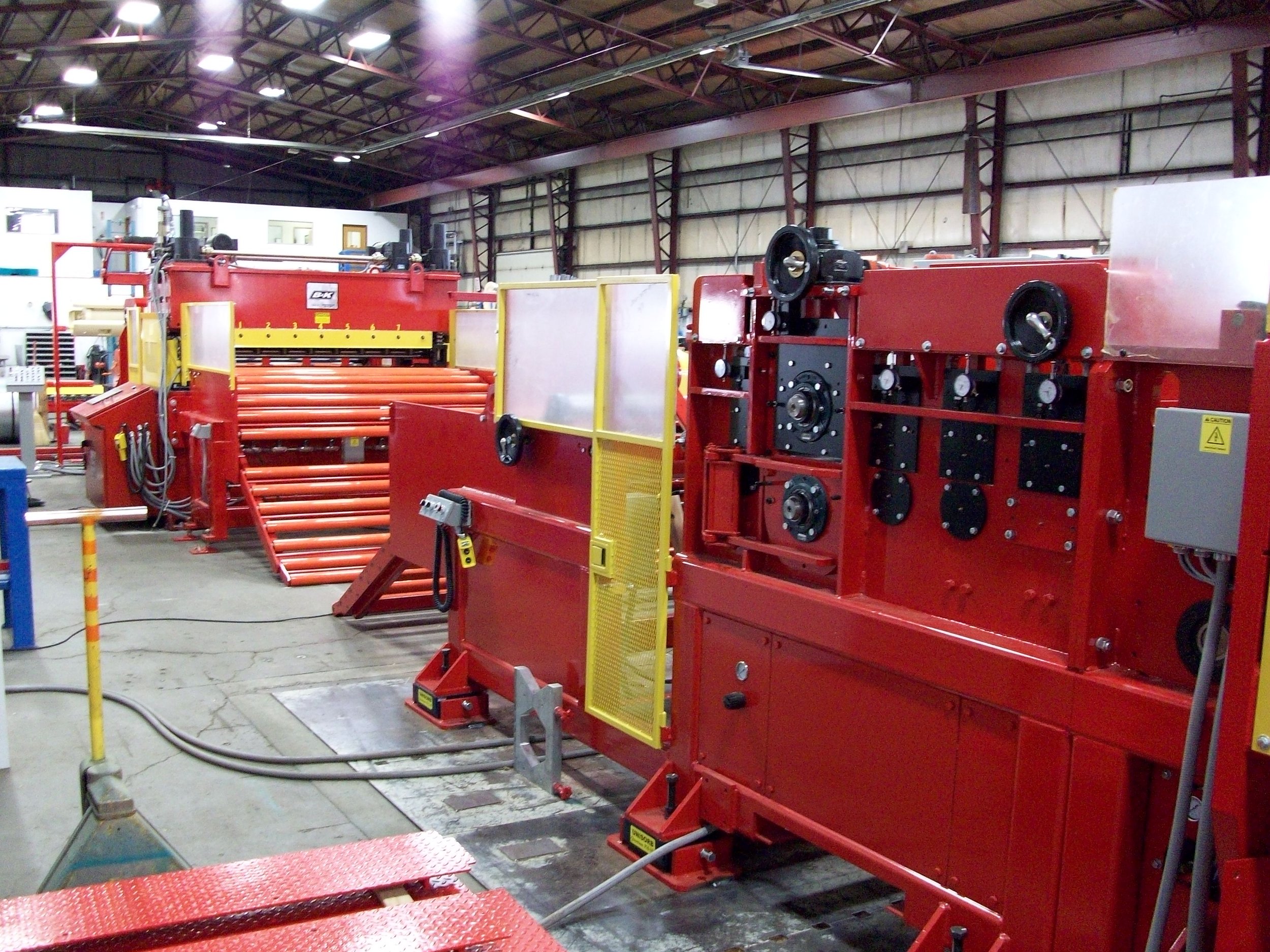 Interior of a factory or warehouse with large red industrial machinery, rollers, and control panels.
