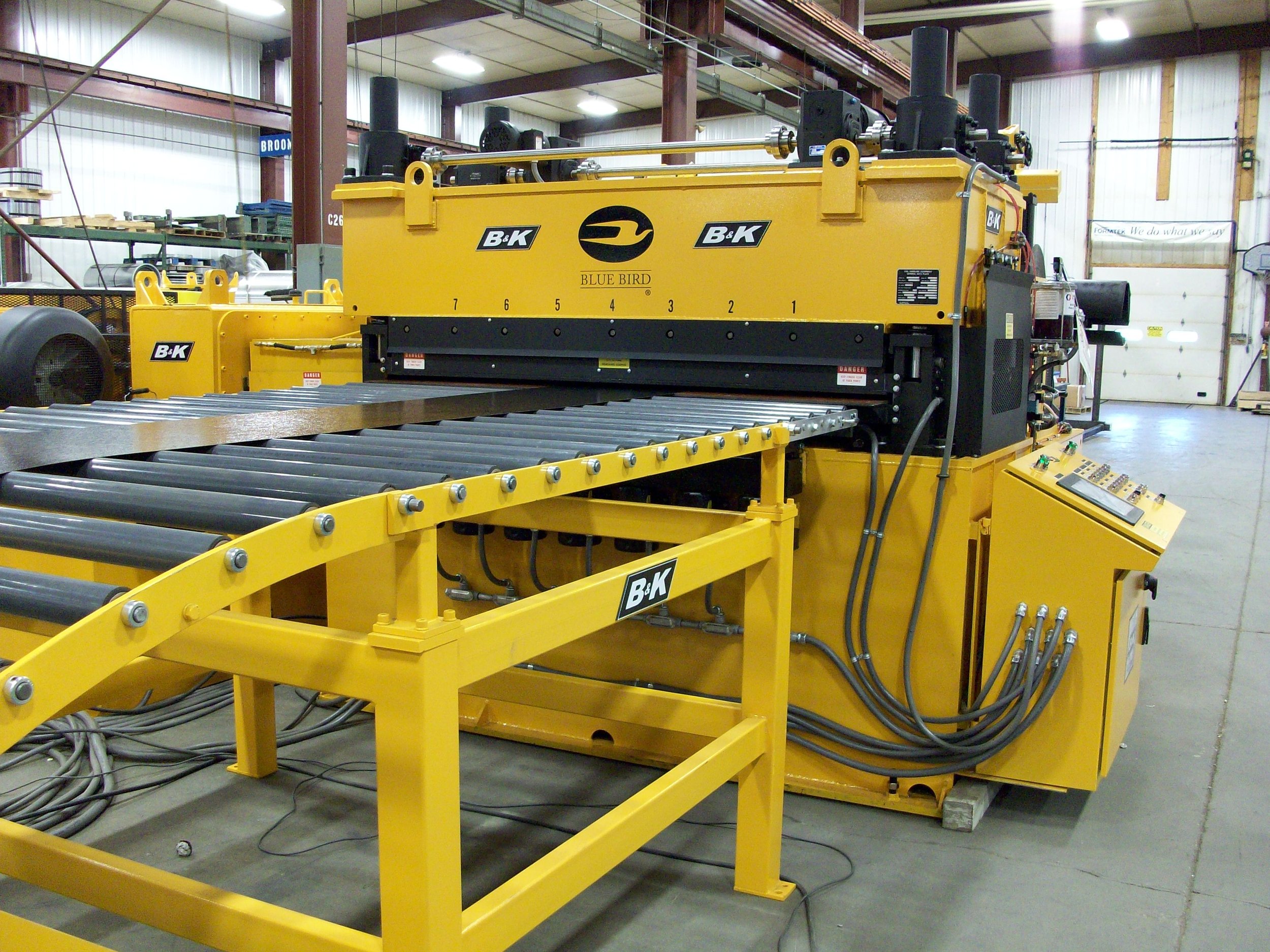 Industrial machine with yellow and black color, labeled B&K and Blue Bird, inside a warehouse.