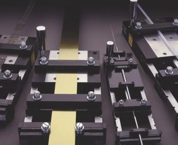 Close-up of a black assembly with metal rods, bolts, and adjustable clamps on a dark surface, likely used for precision positioning or manufacturing.