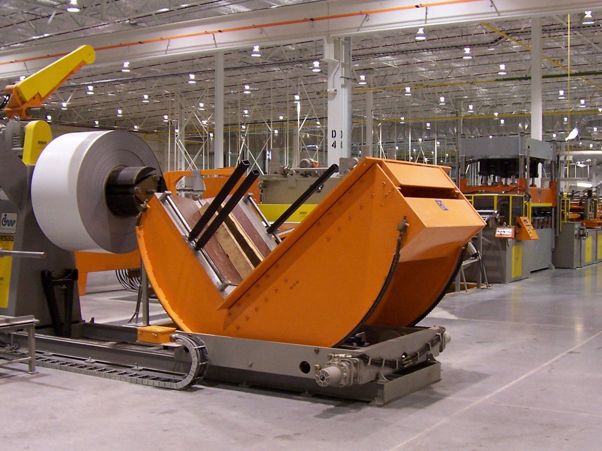 Industrial manufacturing facility with large machinery, including a machine handling a large roll of material and an orange hopper.