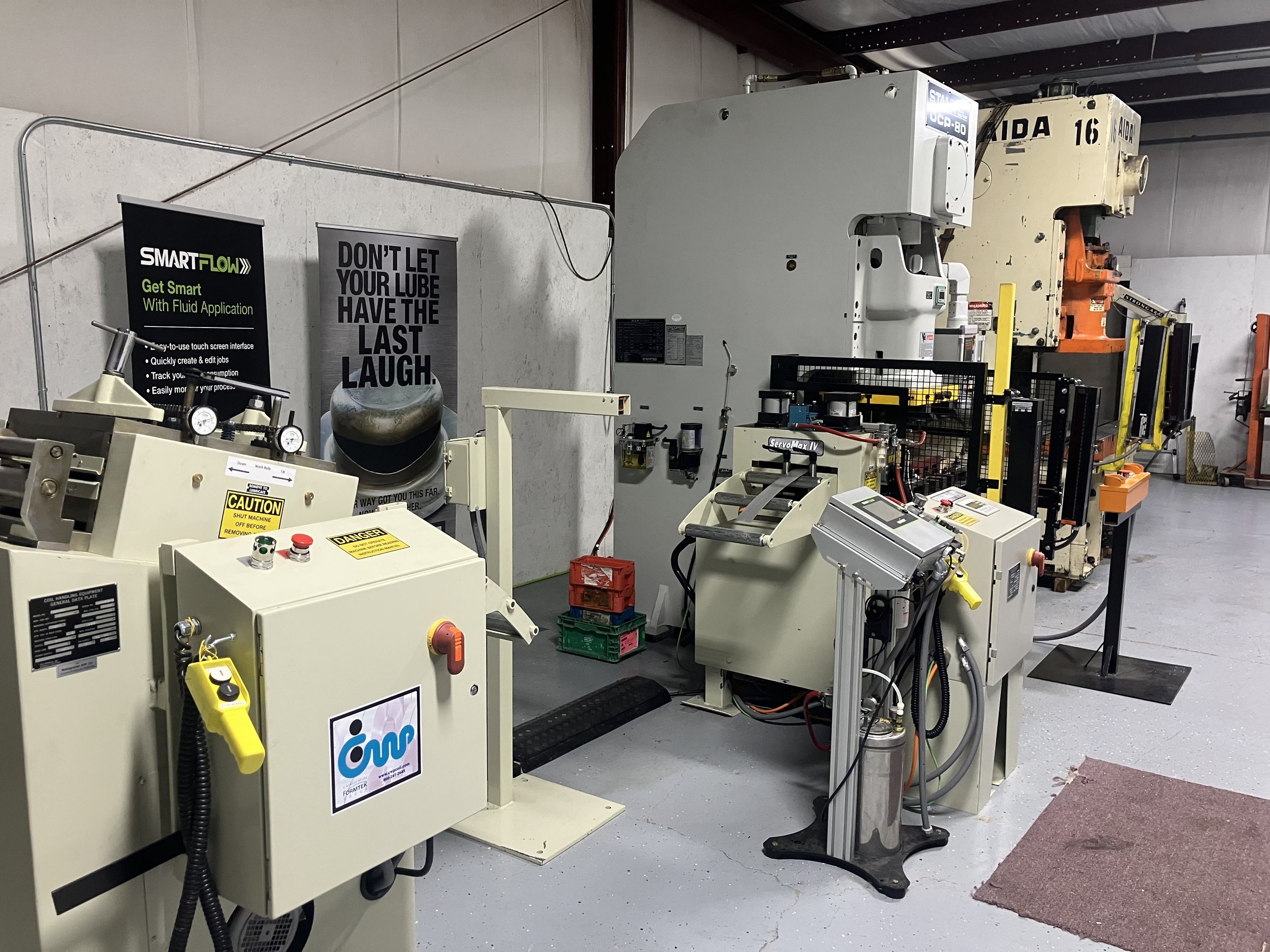 Industrial machinery and equipment in a factory setting with warning labels and posters on the wall.