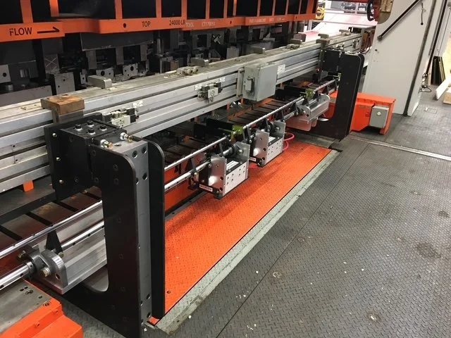 Industrial machinery and equipment in a manufacturing facility, including metal rails, mechanical components, and a safety mat.