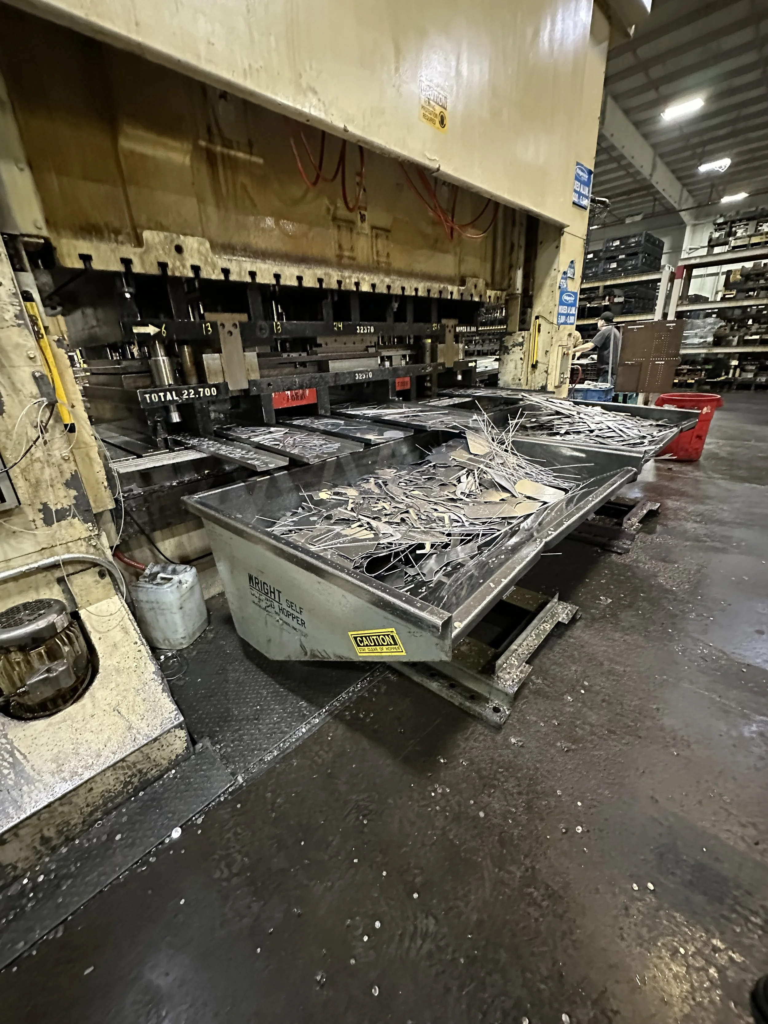 Metal scrap on a stainless steel work table in an industrial warehouse with shelves in the background.