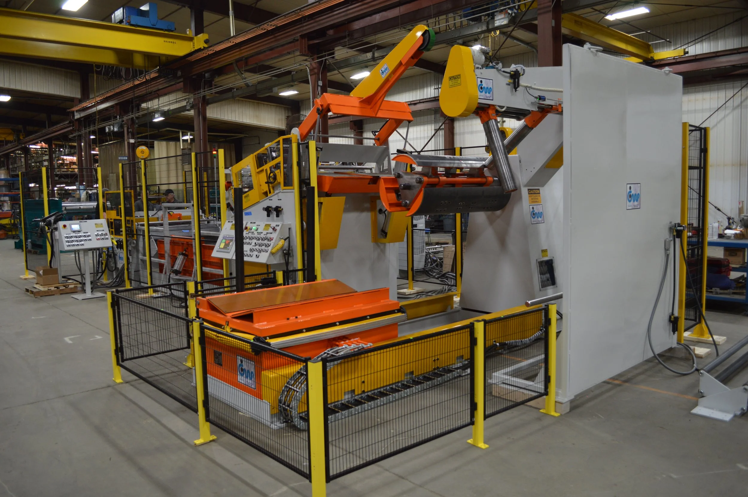 Industrial robotic machinery inside factory with safety fencing and control panels.