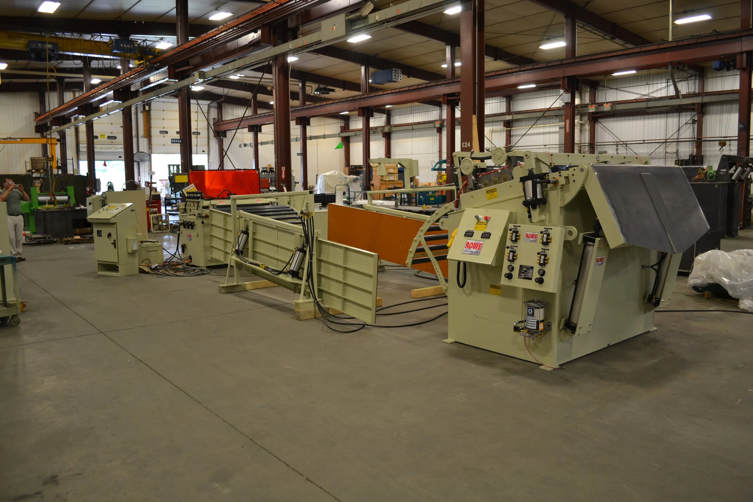 Industrial factory floor with large sheet metal forming machine and various tools and equipment, with a person taking a photo on the left