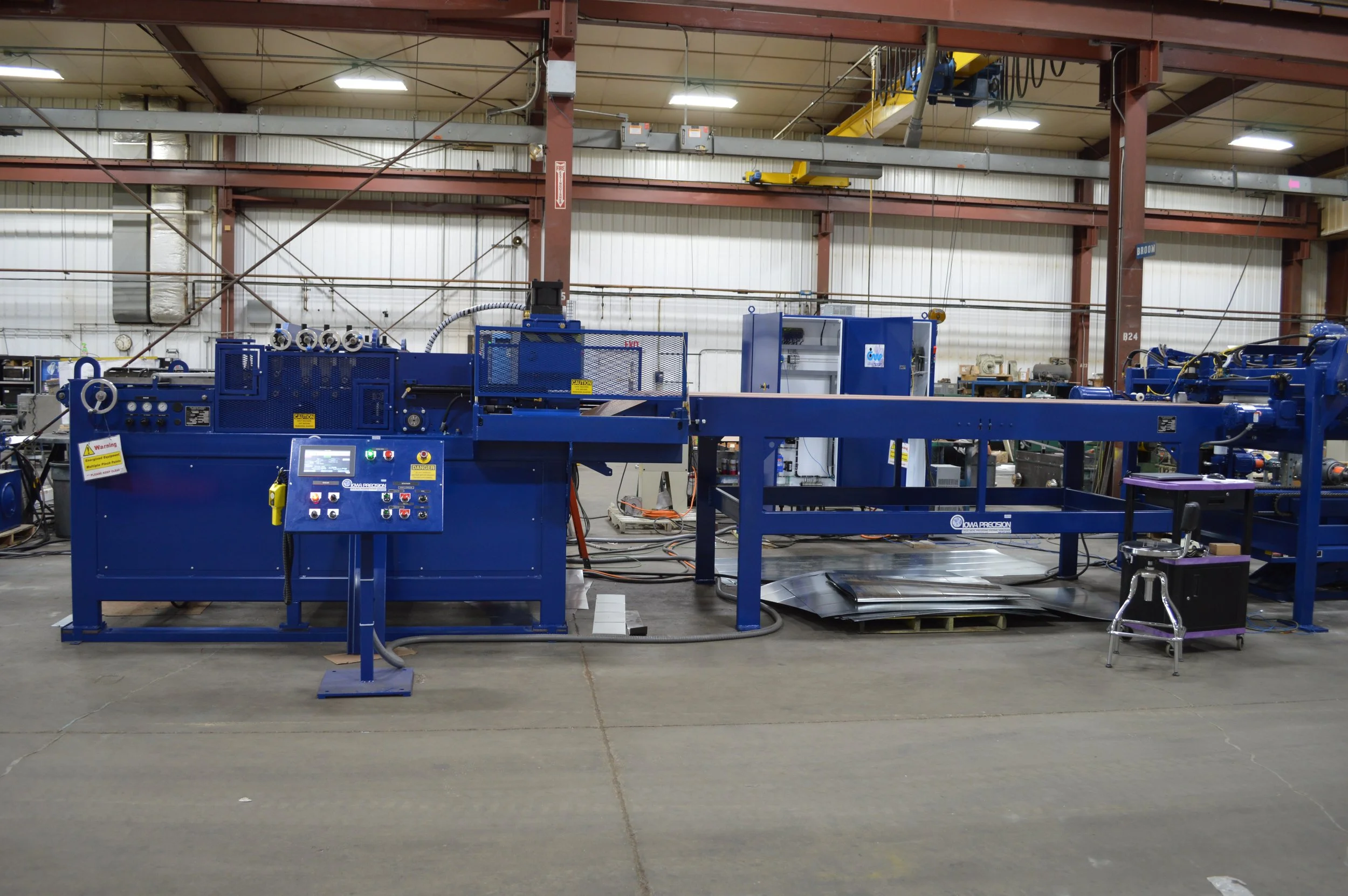 Industrial manufacturing machine in a factory setting with control panel, industrial equipment, and safety signs.