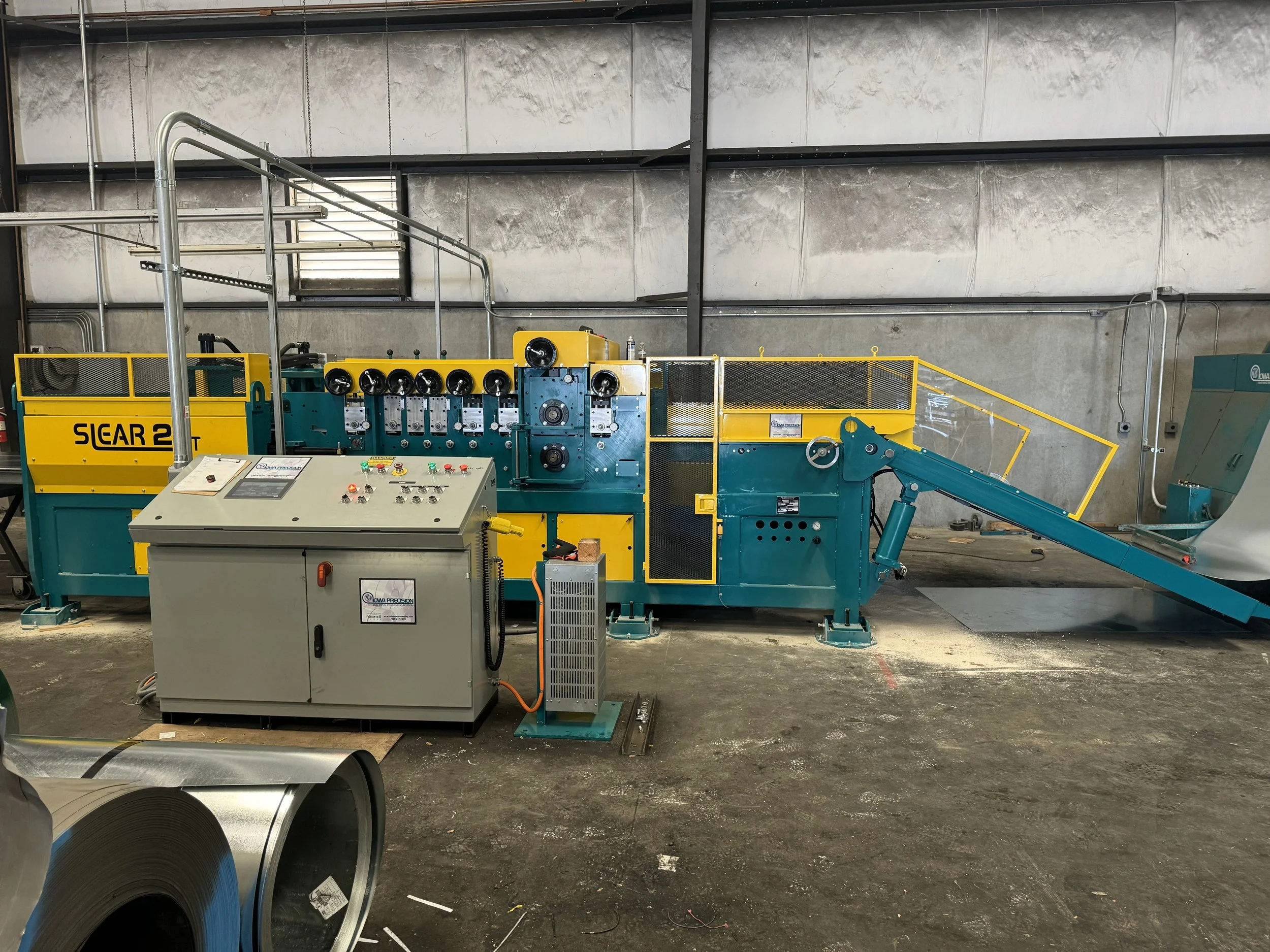 Industrial machine with control panel, yellow and blue components, and a conveyor belt in a factory setting.