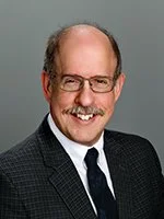 A middle-aged man with glasses and a beard, wearing a dark suit and tie, smiling for the camera.