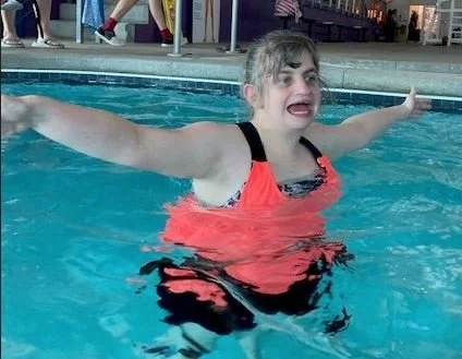 A young girl swimming in a pool with arms extended outward.
