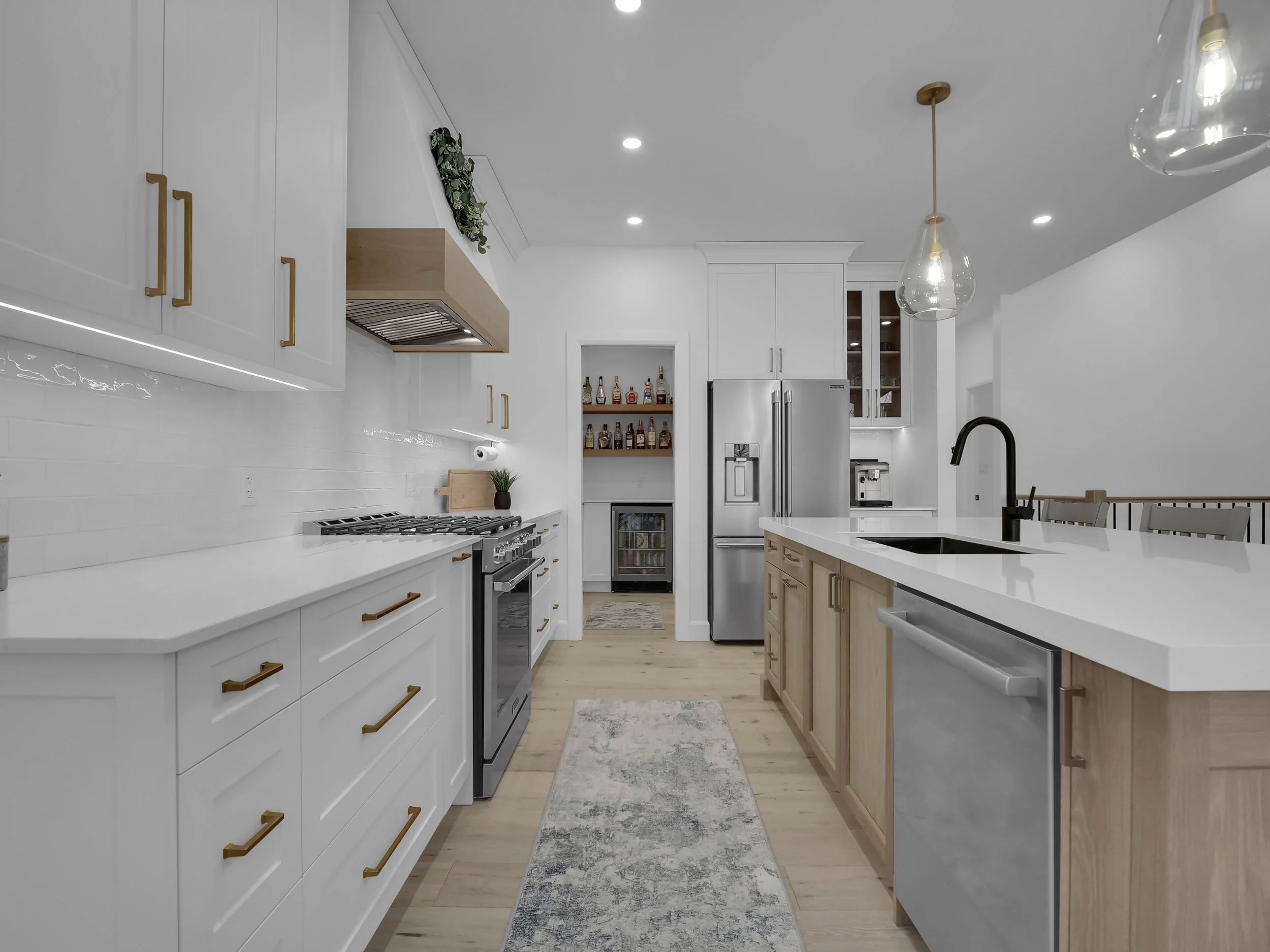 Modern kitchen with white cabinets, a kitchen island with a white countertop, stainless steel appliances, pendant lights, and light wood flooring.