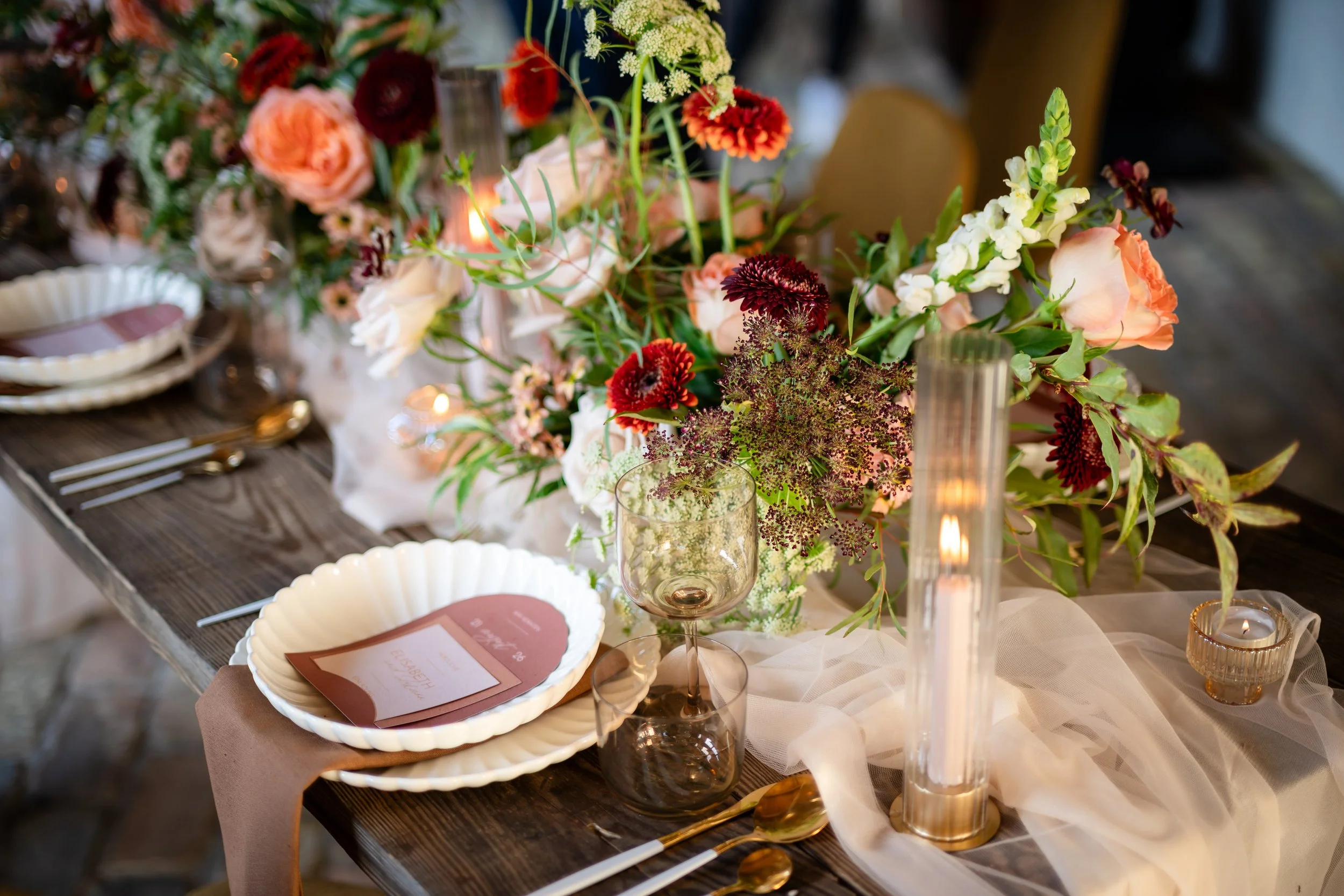 Ein festlich gedeckter Tisch mit einer großen Blumenarrangement, Kerzen, Geschirr, Gläsern und Besteck für eine Hochzeit in Brandenburg. Aufgenommen von Hochzeitsfotograf Dominic Glock.
