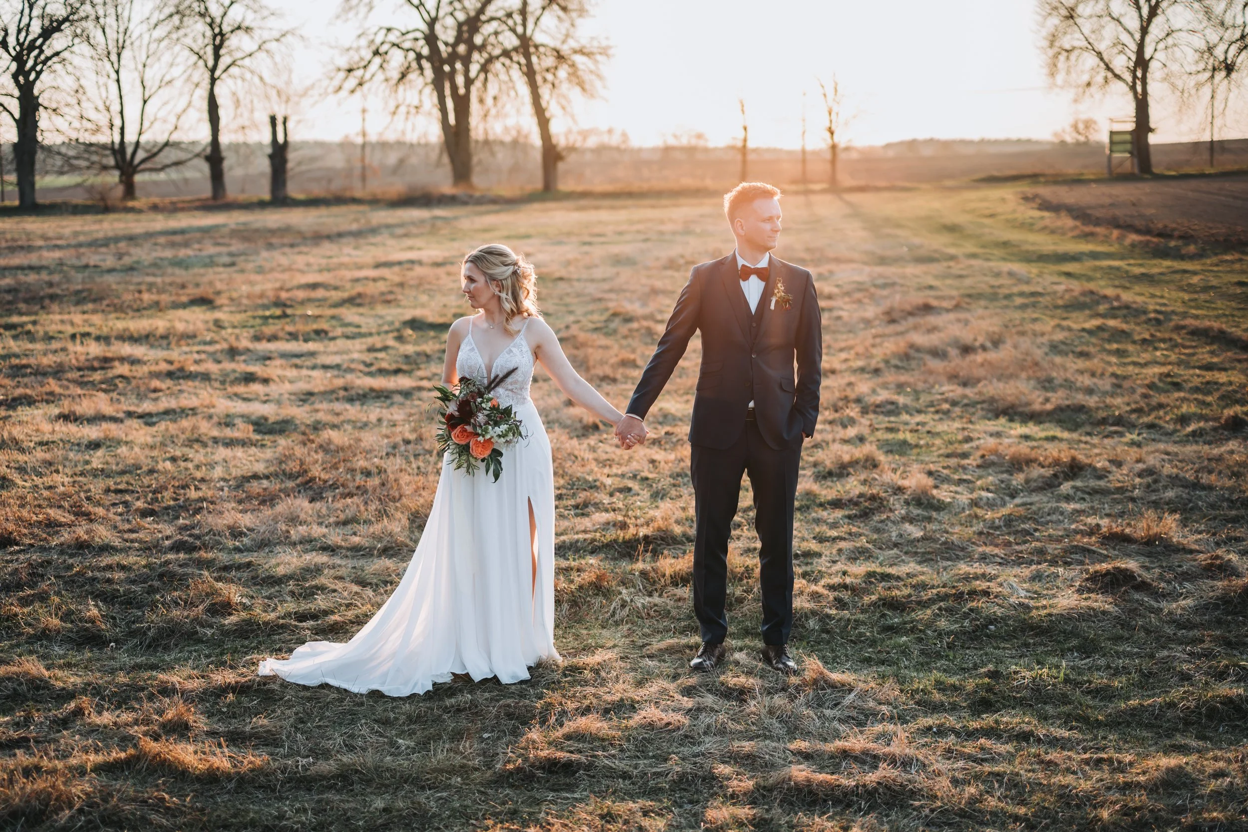 Ein Hochzeitspaar steht auf einem Feld in Brandenburg bei Berlin. Braut und Bräutigam halten sich an der Hand und schauen in unterschiedliche Richtungen.