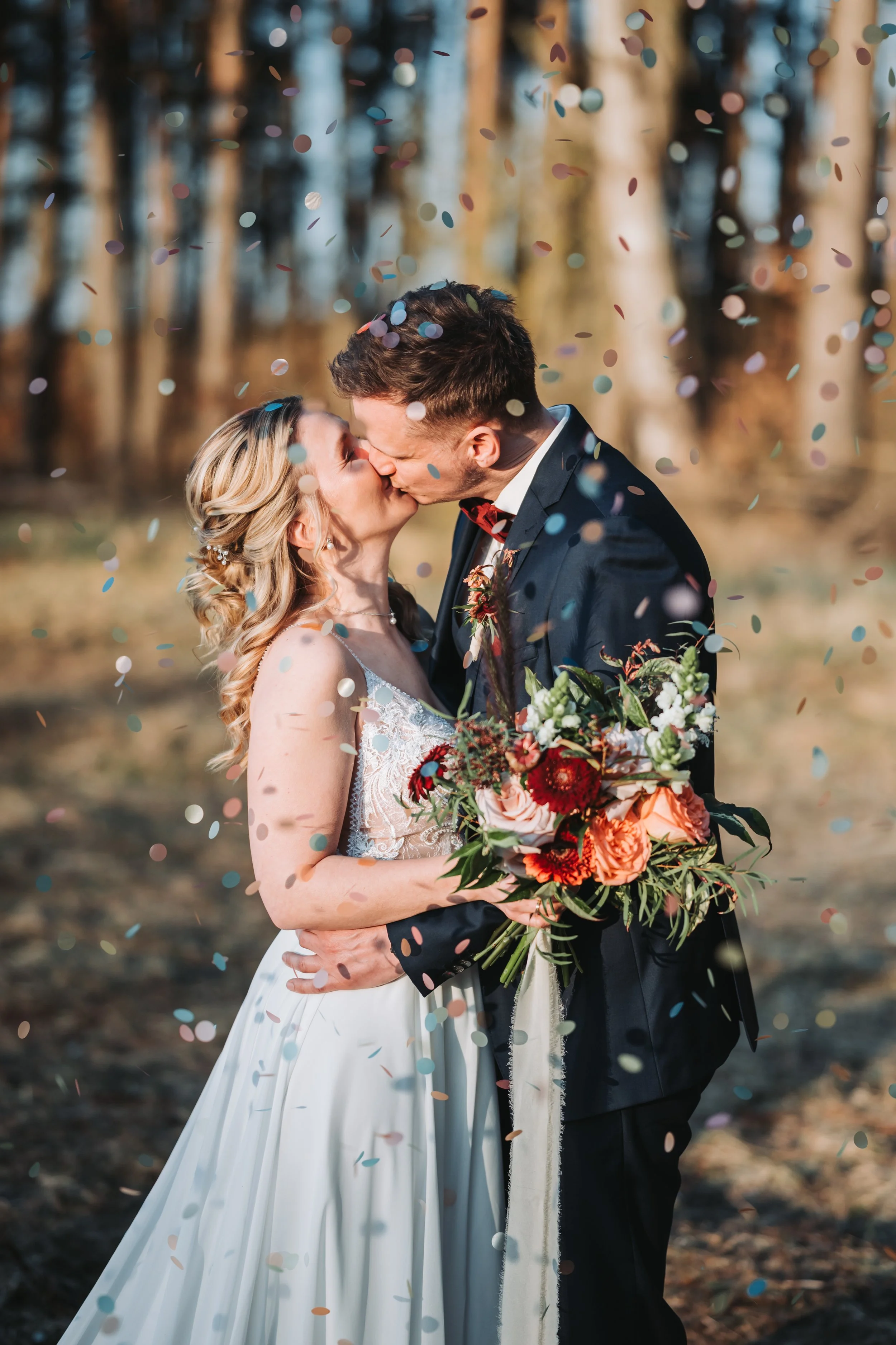 Ein Brautpaar küsst sich während einer Hochzeit im Freien, umgeben von fallendem Konfetti und Bäumen im Hintergrund. Aufgenommen von Hochzeitsfotograf Dominic Glock.