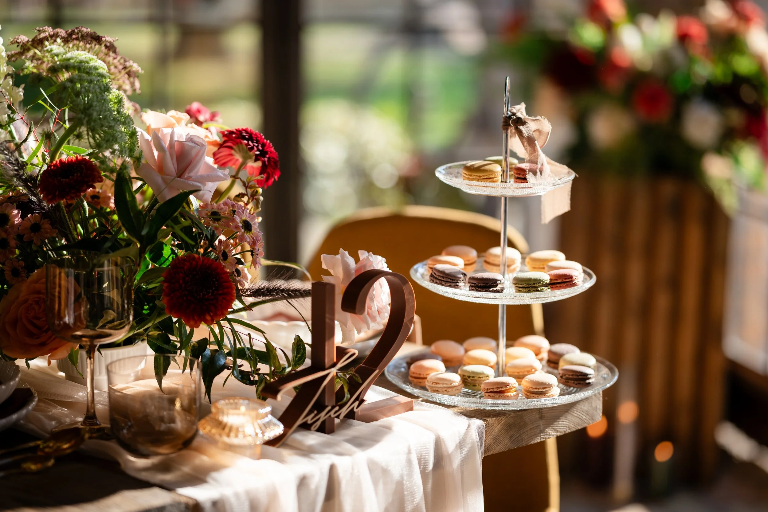 Ein Tisch mit bunten Macarons, einer Blumenbouquet, Kerzen und dekorativen Elementen bei einer Hochzeitsfeier in Brandenburg. Aufgenommen von Hochzeitsfotograf Dominic Glock.