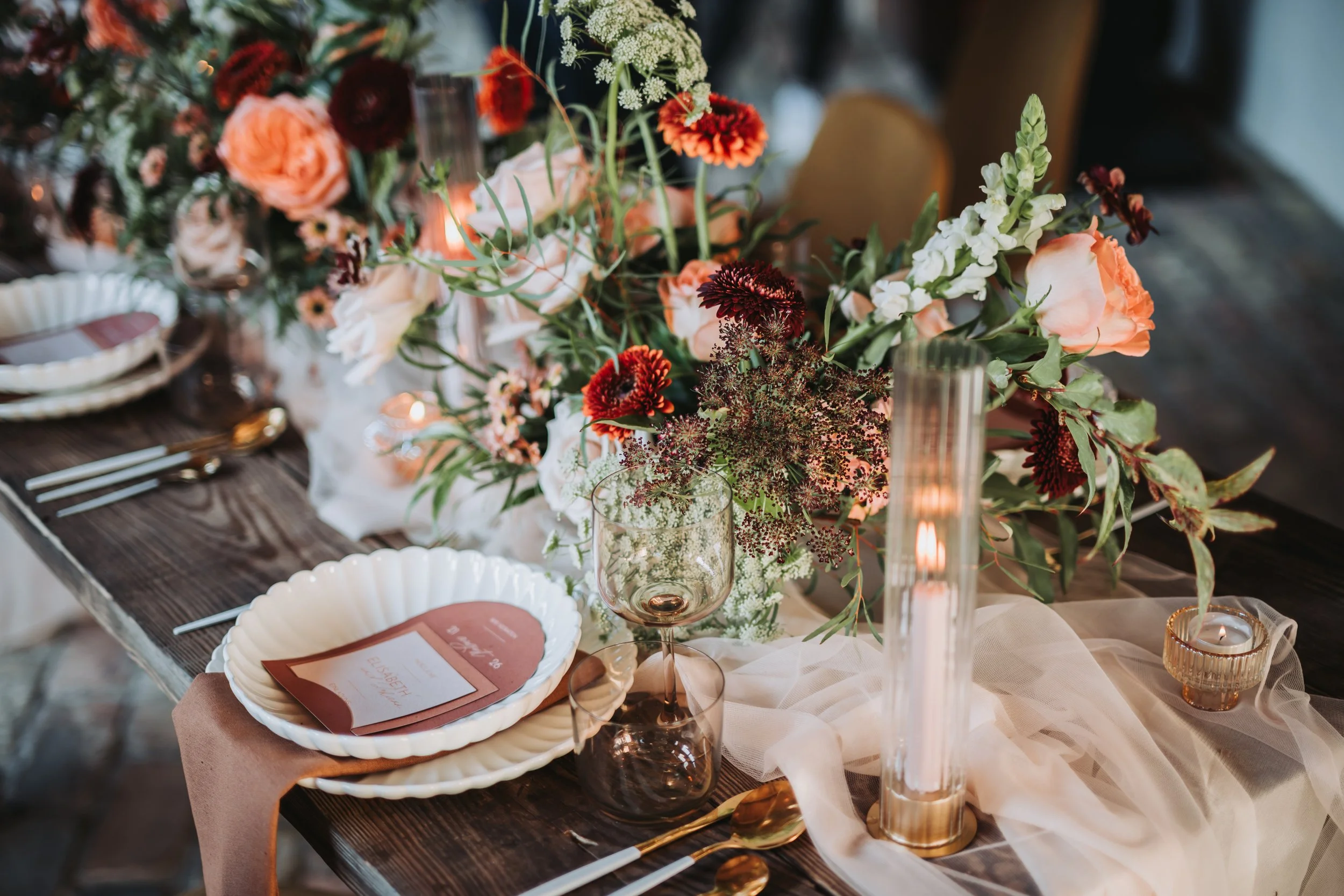 Ein festlich gedeckter Tisch mit einer großen Blumenarrangement, Kerzen, Geschirr, Gläsern und Besteck für eine Hochzeit in Brandenburg. Aufgenommen von Hochzeitsfotograf Dominic Glock.