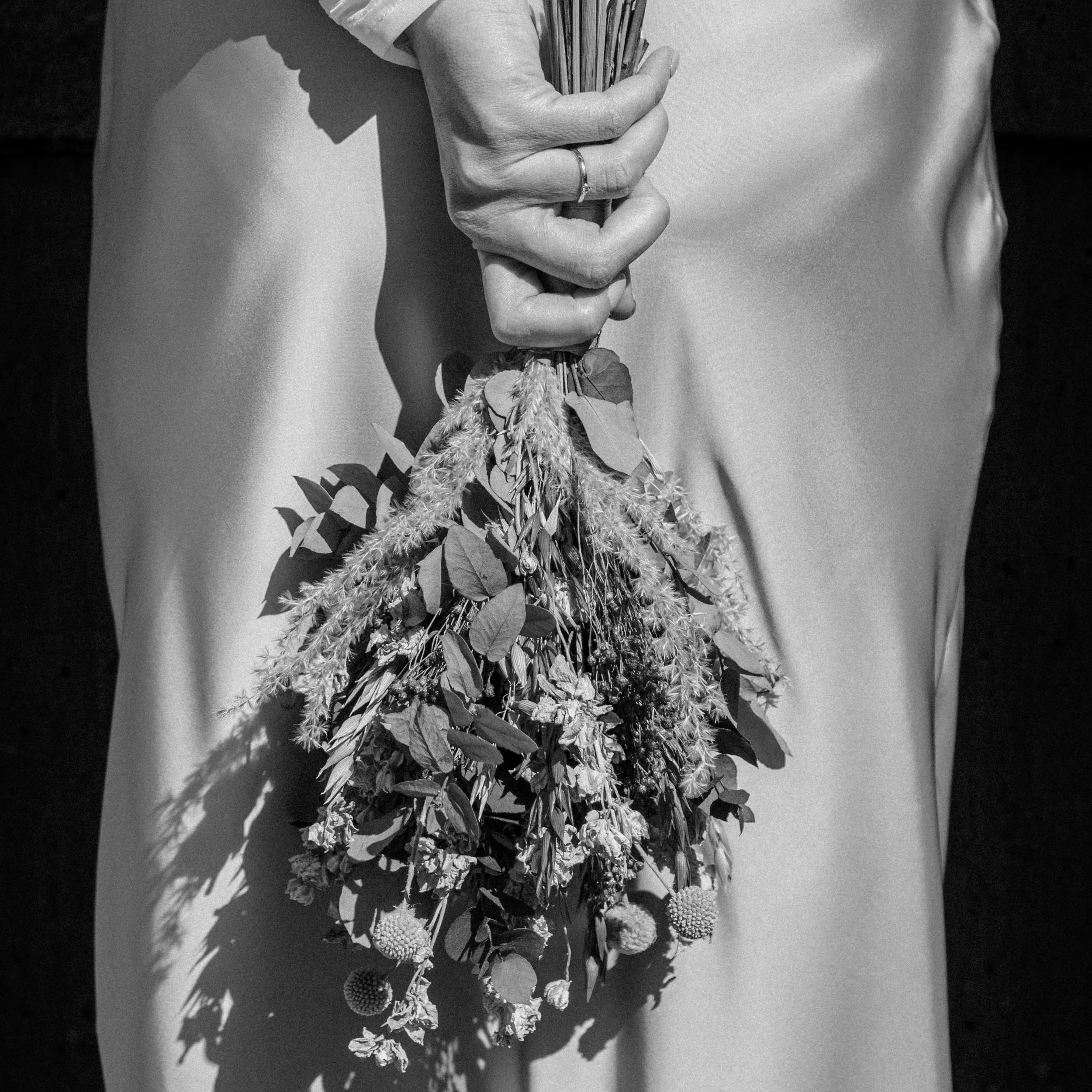 Schwarz-Weiß-Fotografie einer Braut von hinten. Man sieht den Brautstrauß vor dem Hochzeitskleid.