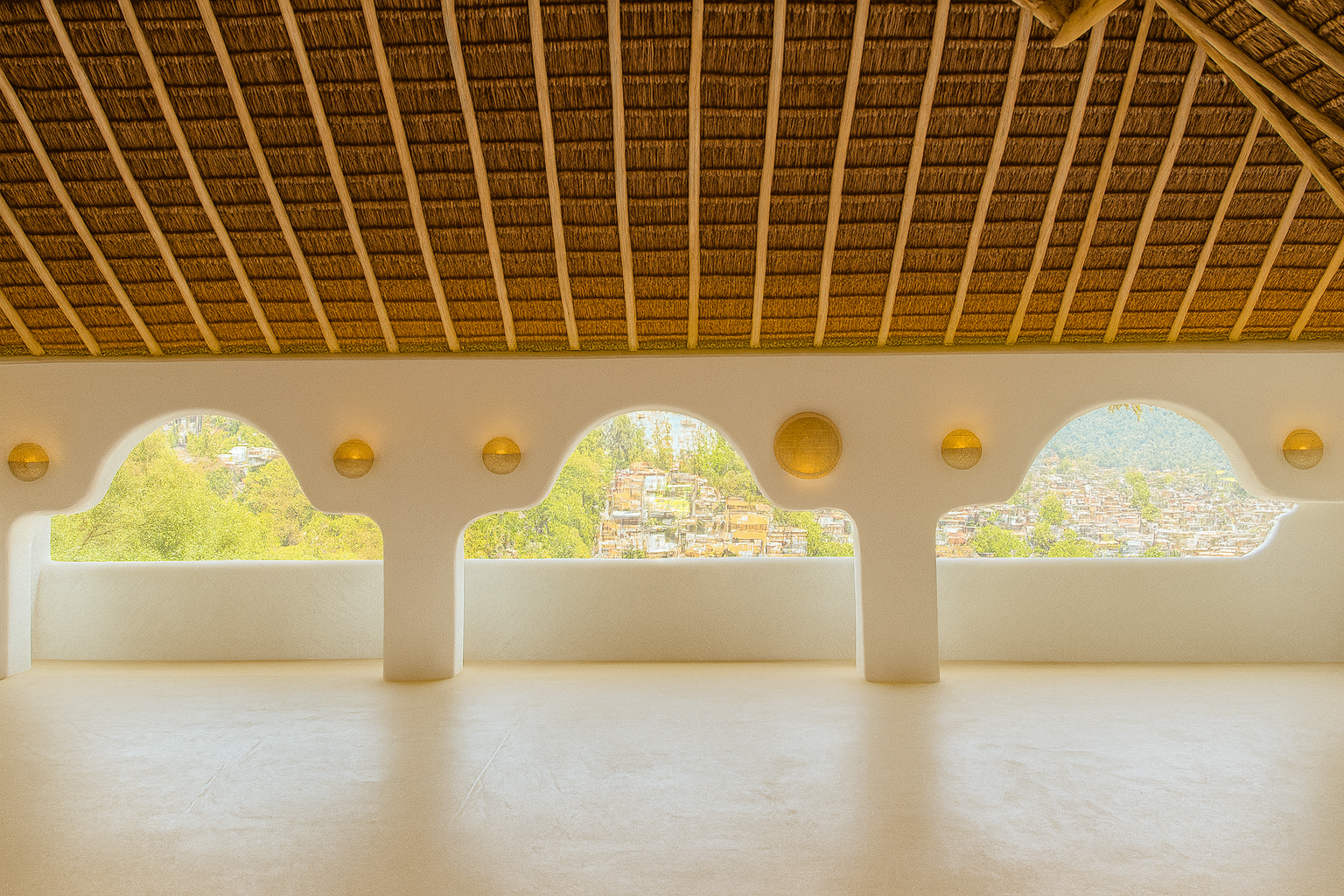 Open balcony with decorative openings and natural view, featuring a thatched roof ceiling and minimalistic white walls.