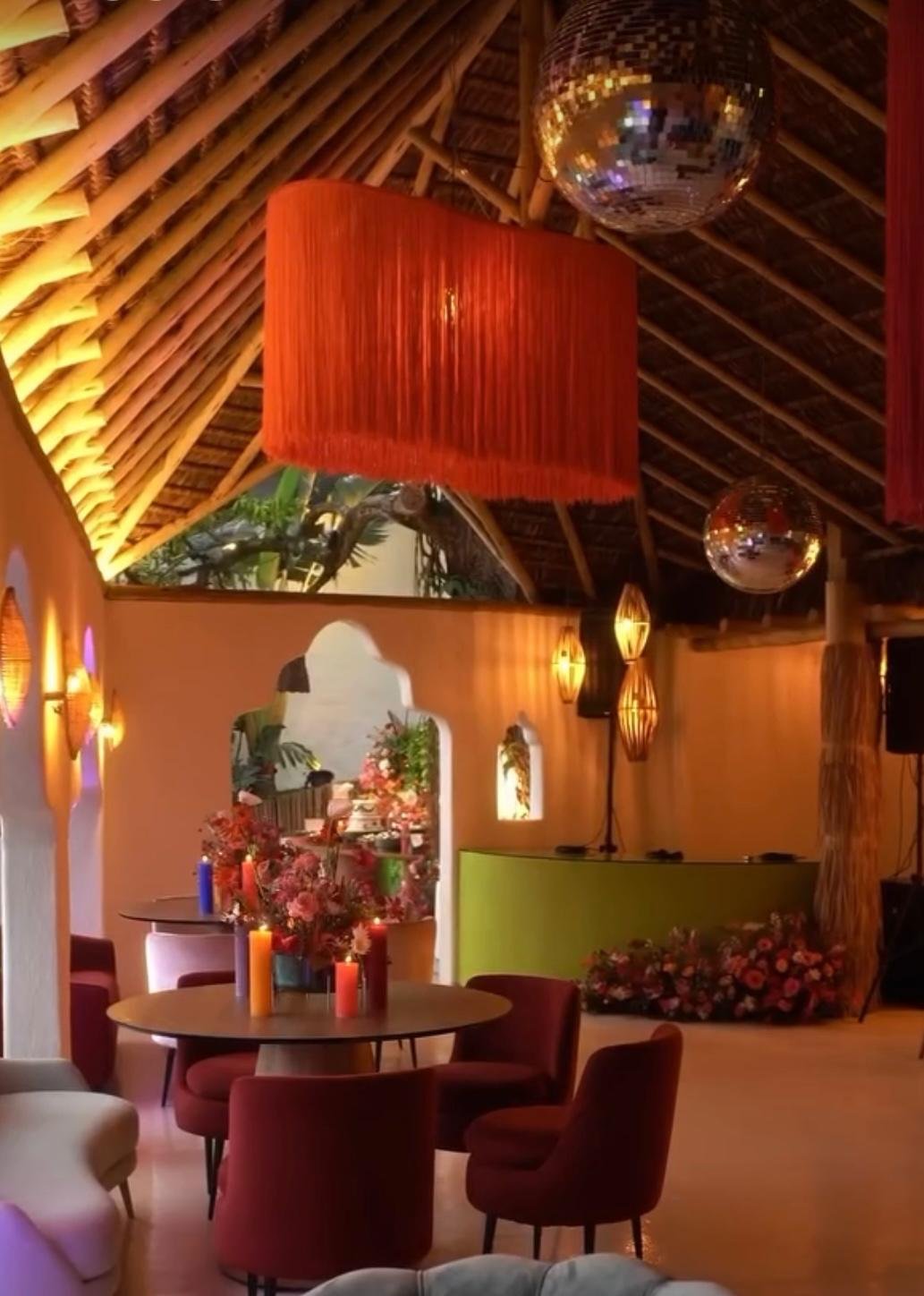 Interior of a decorated venue with round tables, chairs, large hanging red lampshade, disco balls, and floral arrangements.