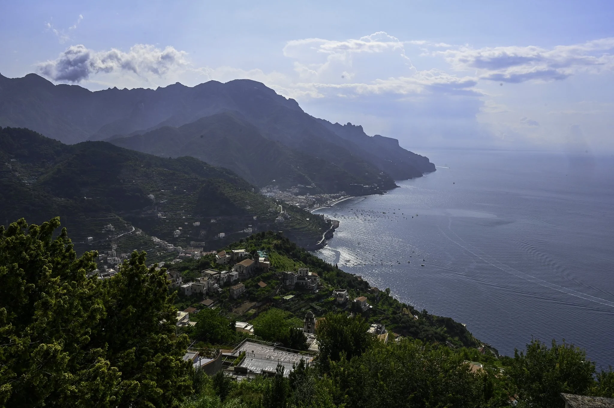 Coastal town nestled in green hills with mountains in the background and the ocean extending into the horizon.