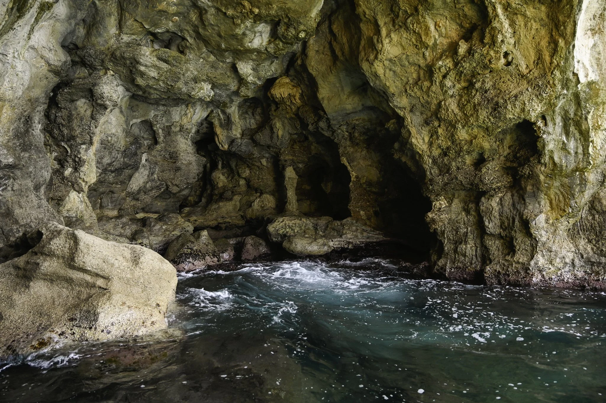 A rocky ocean cave with blue water entering through an opening in the cave wall.