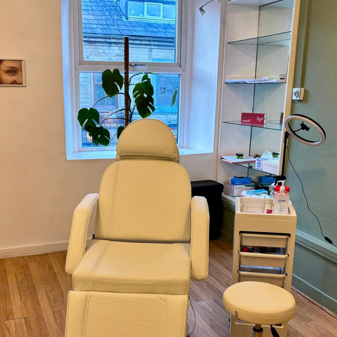 Calm permanent makeup treatment room featuring a cream reclining chair, treatment stool, and equipment in a clean professional space.