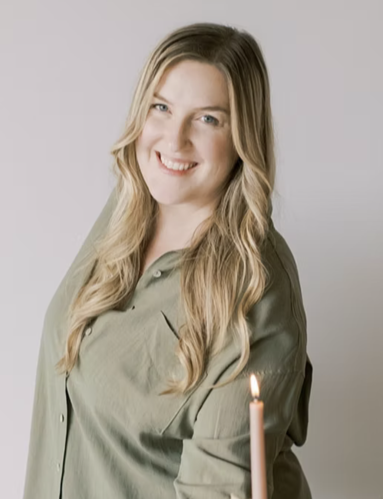 A woman with long blonde hair wearing a light green shirt, smiling, with a lit pink candle in the foreground.