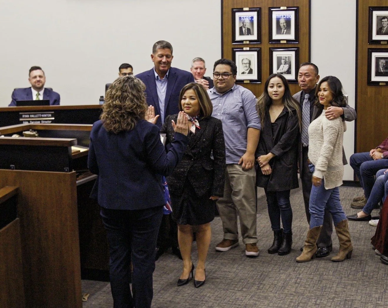A group of people standing in a courtroom or official setting, taking an oath or participating in a swearing-in ceremony, with a judge or official overseeing the event.