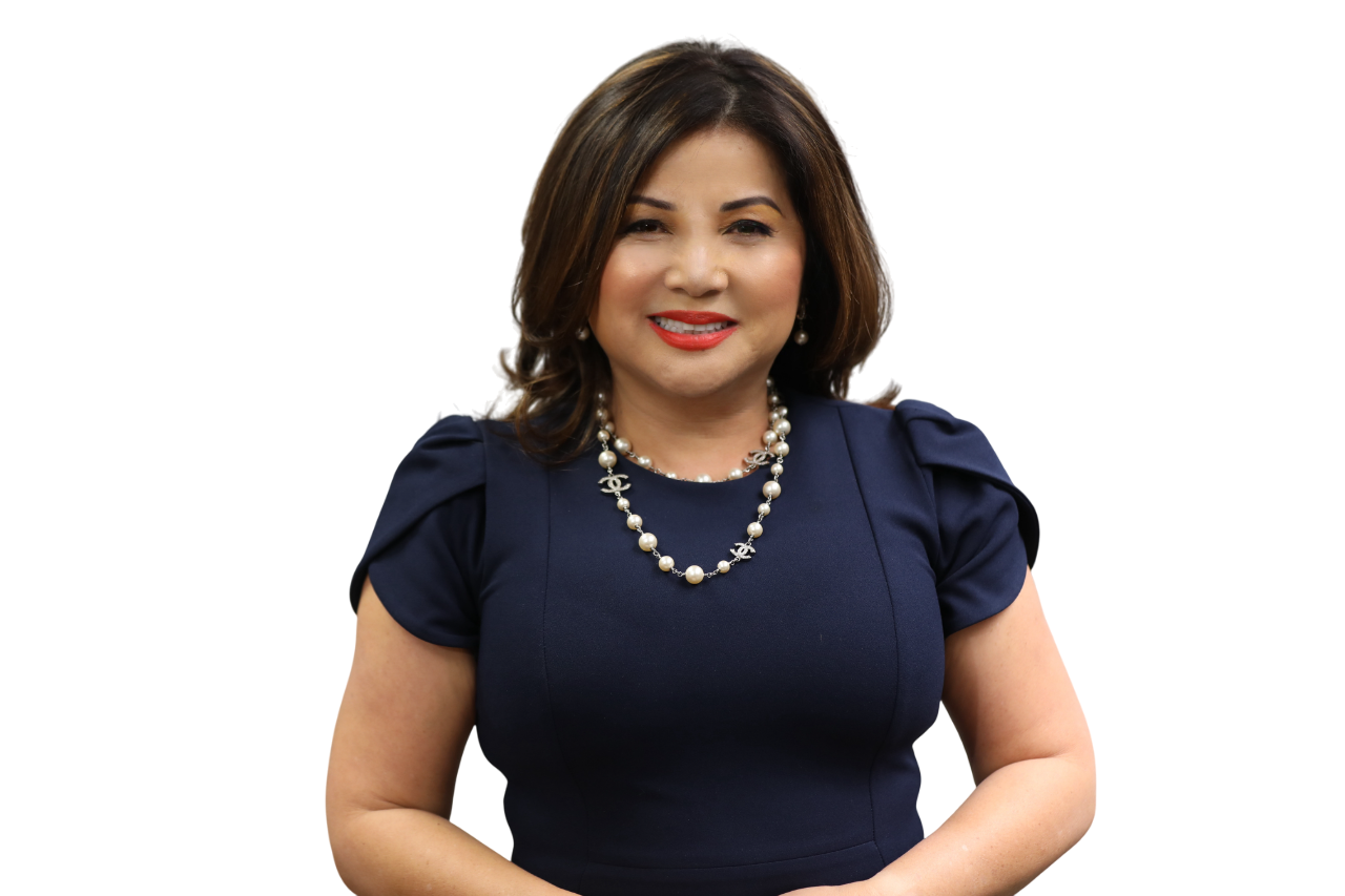 A woman with shoulder-length hair, wearing a navy blue dress, pearl jewelry, and red lipstick, smiling at the camera.