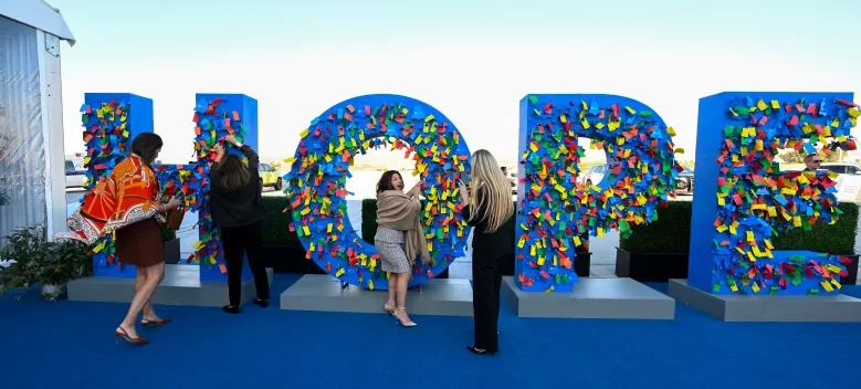 Large blue letters spelling "HOPE" decorated with colorful sticky notes, with several people attaching notes to the letters at an outdoor event.