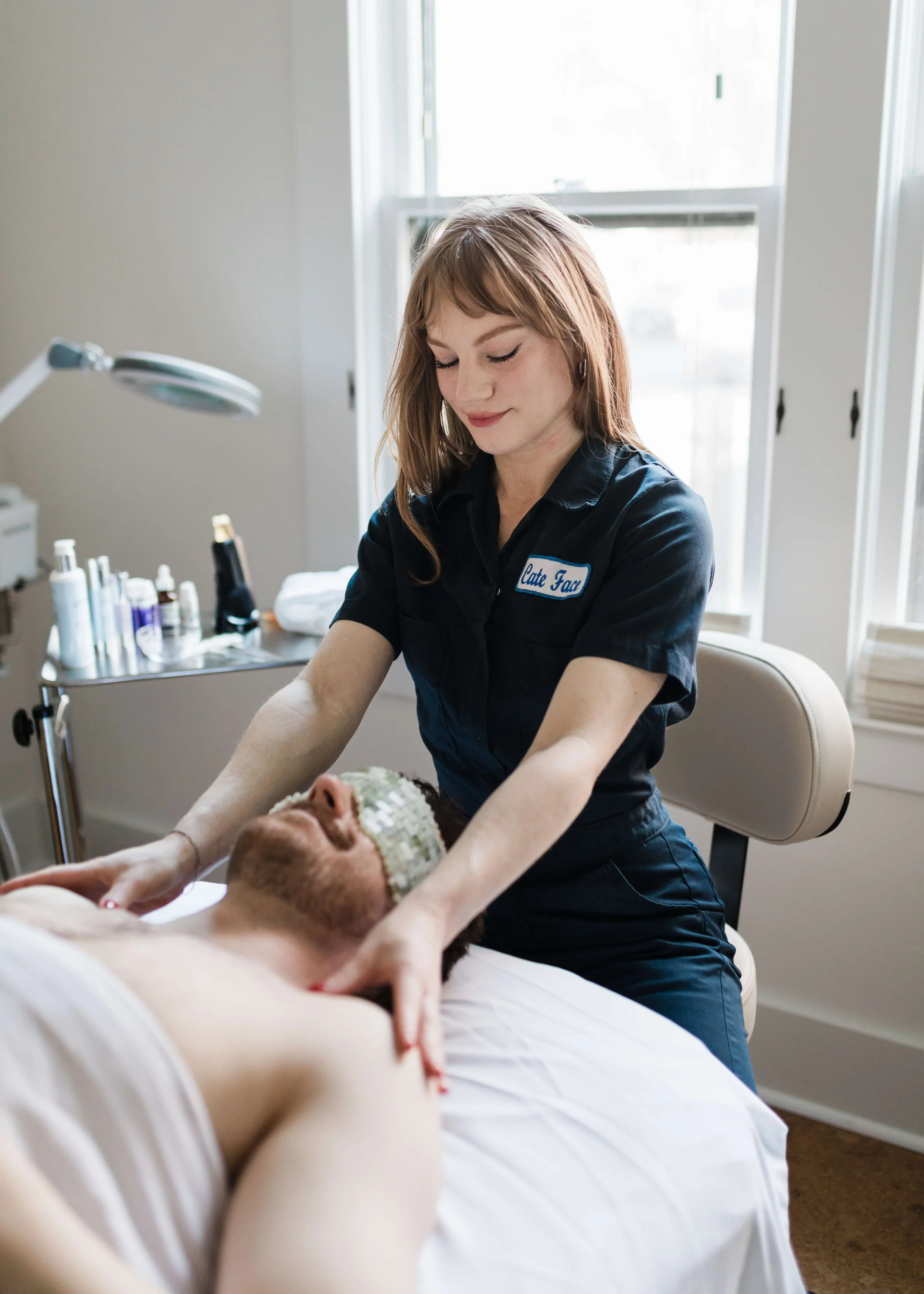 A person is lying down on a massage table and is receiving a facial treatment from Cate Draney, Portland Esthetician, in a private treatment room.