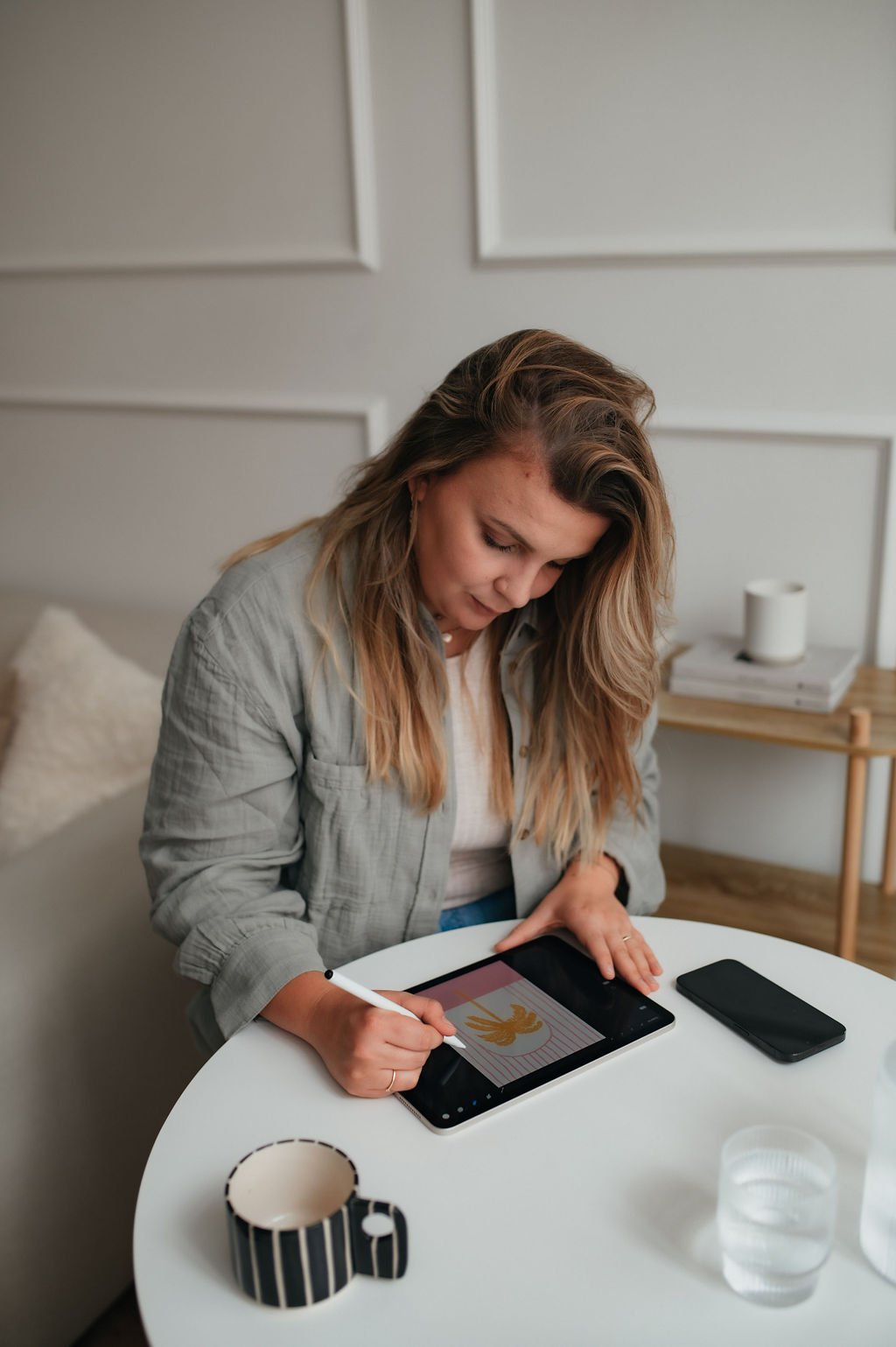 A woman drawing a bird on a tablet with a stylus at a white round table.