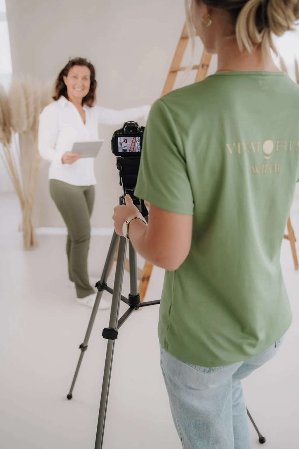 A woman filming another woman in a white shirt holding a tablet in a photo studio.