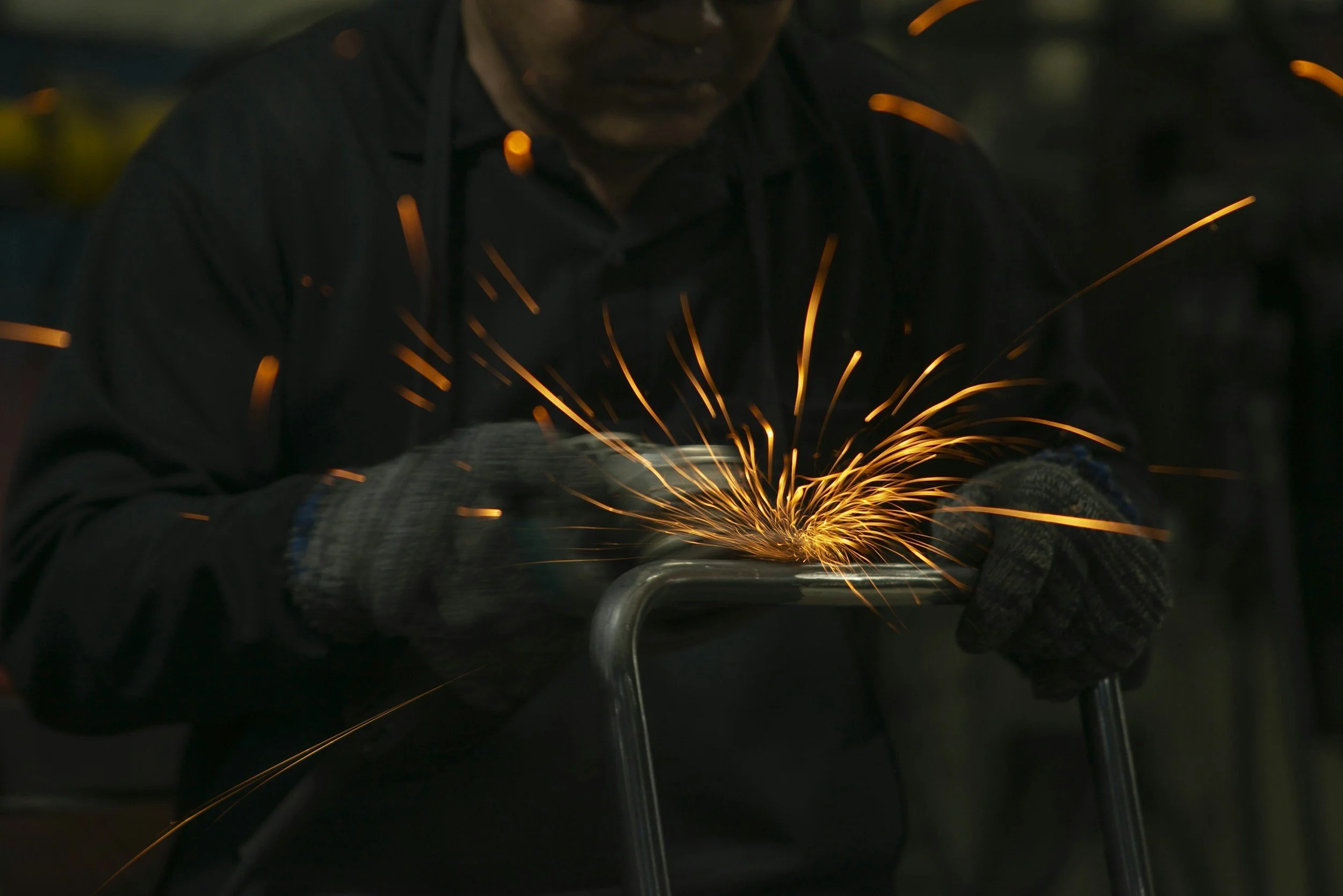 A person welding metal, with sparks flying as the welder works on a metal object in a dark environment.