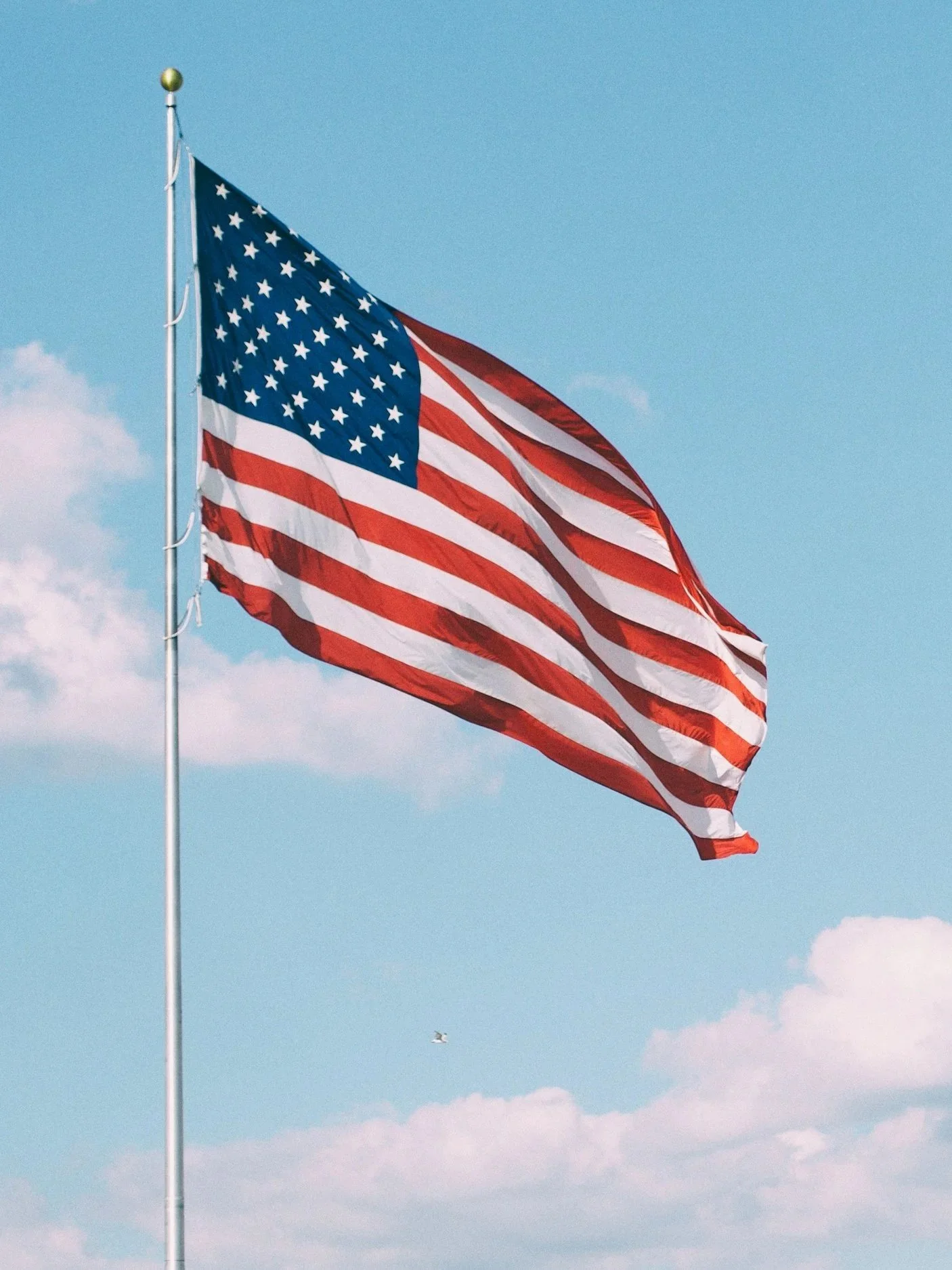 American flag waving in the wind against a blue sky with some clouds.