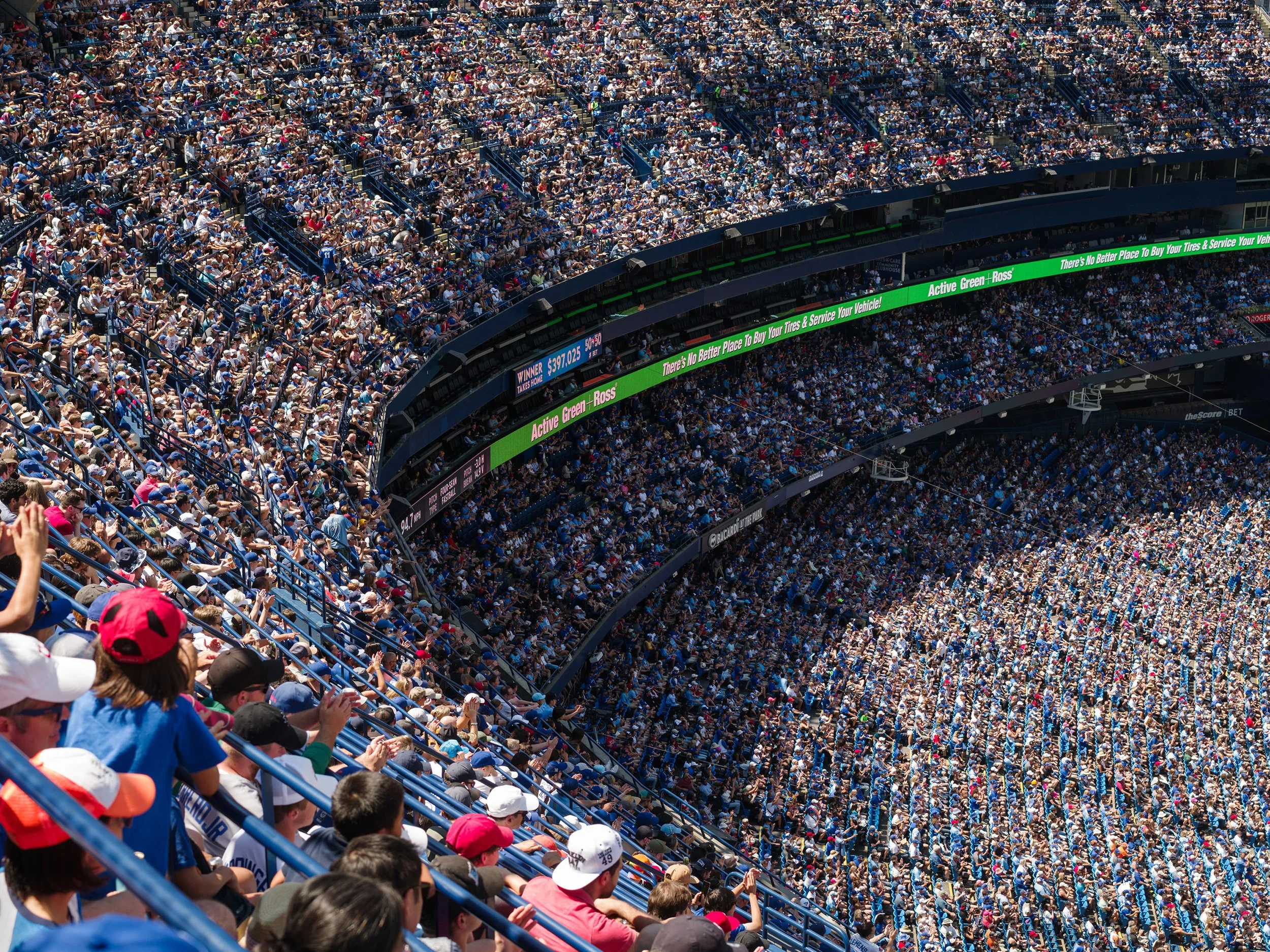 Crowd of spectators in a stadium, some wearing hats and baseball caps, watching a game or event.