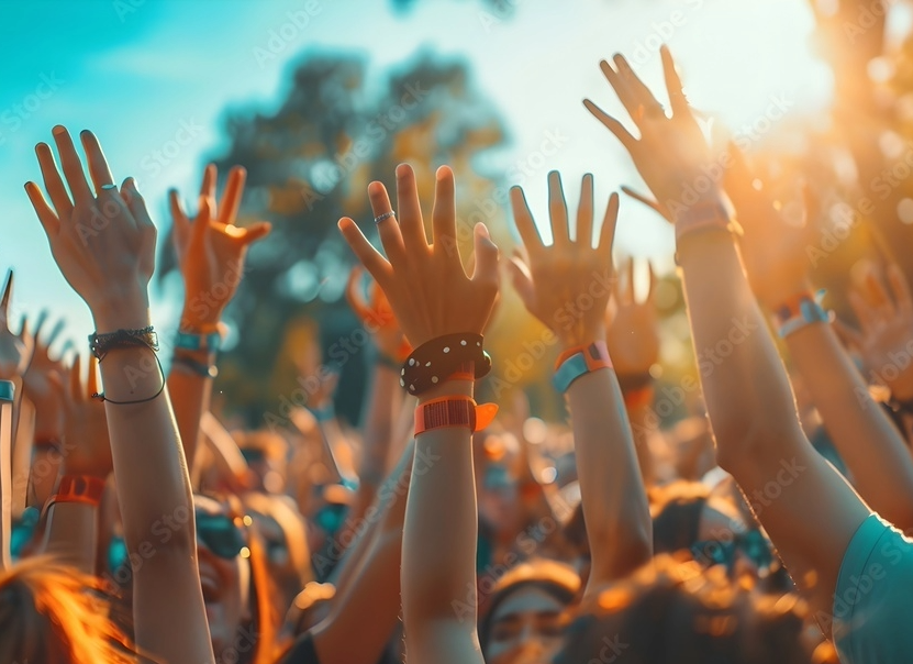 Crowd of people with hands raised at an outdoor event during sunset.