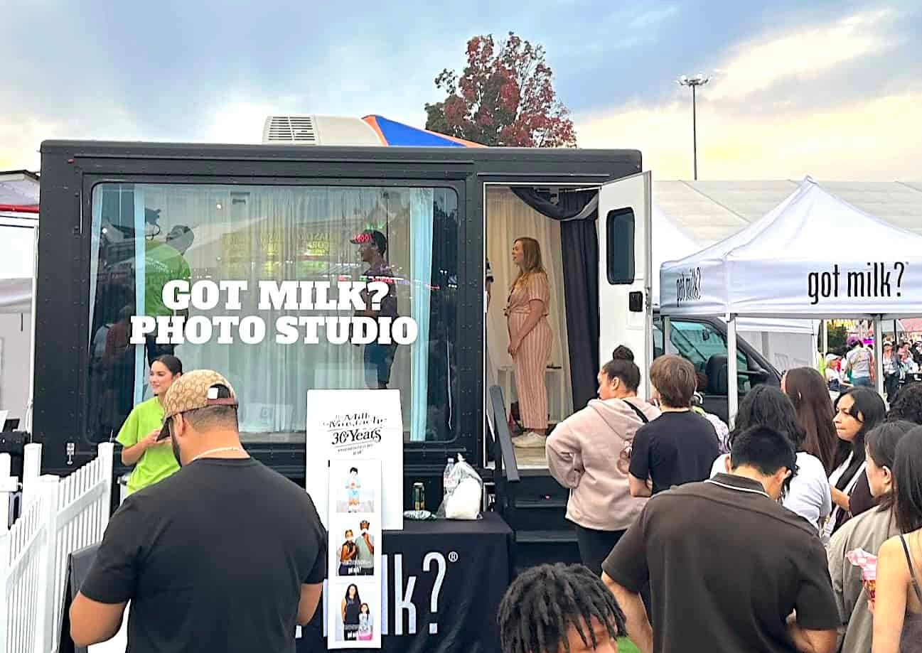 People attending a photo booth at an outdoor event, with a large truck and a white tent labeled "got milk?" next to the booth.
