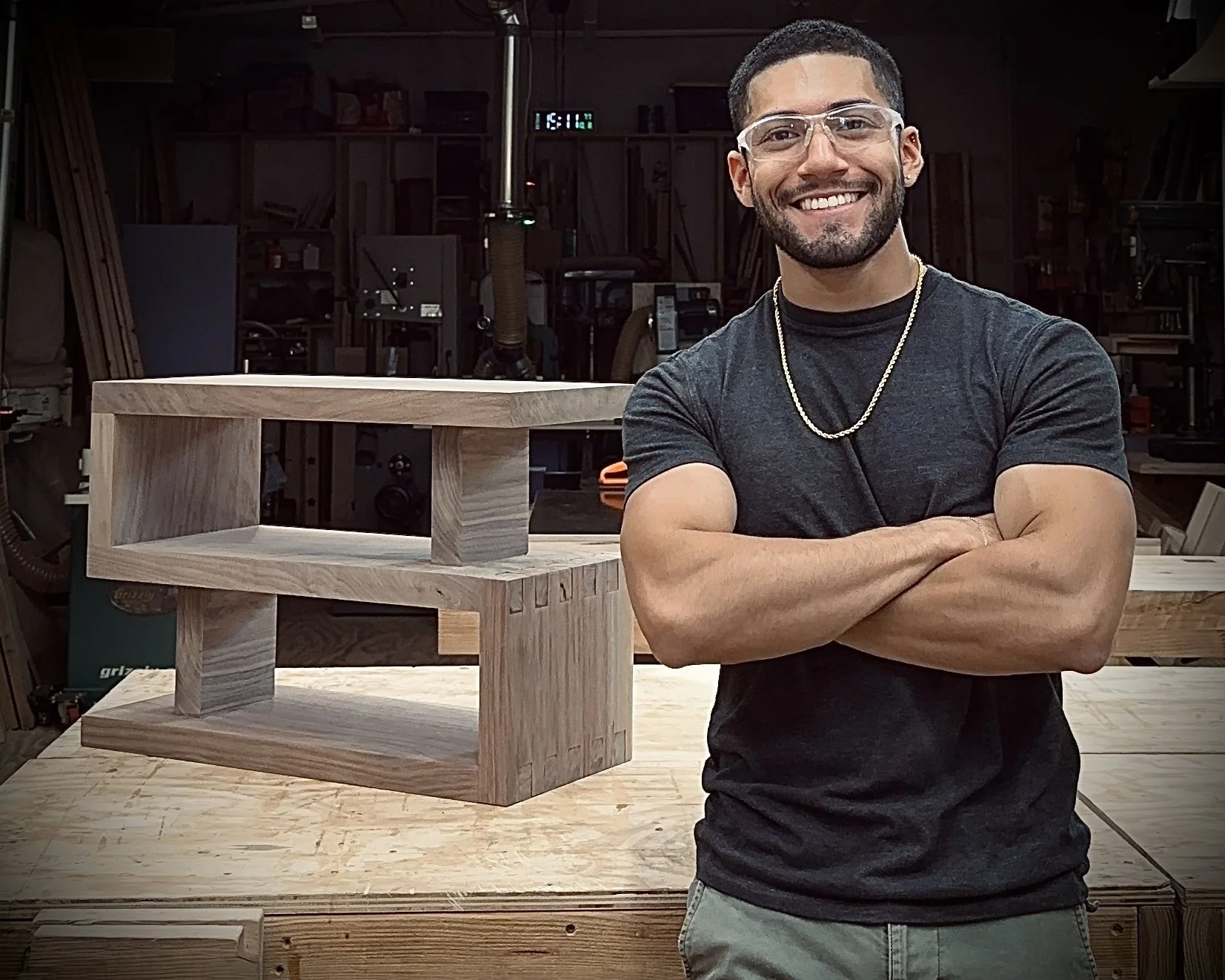 Jefferson Acevedo, founder of J.S. Made, standing in his New York woodworking studio beside a handcrafted solid wood geometric table.