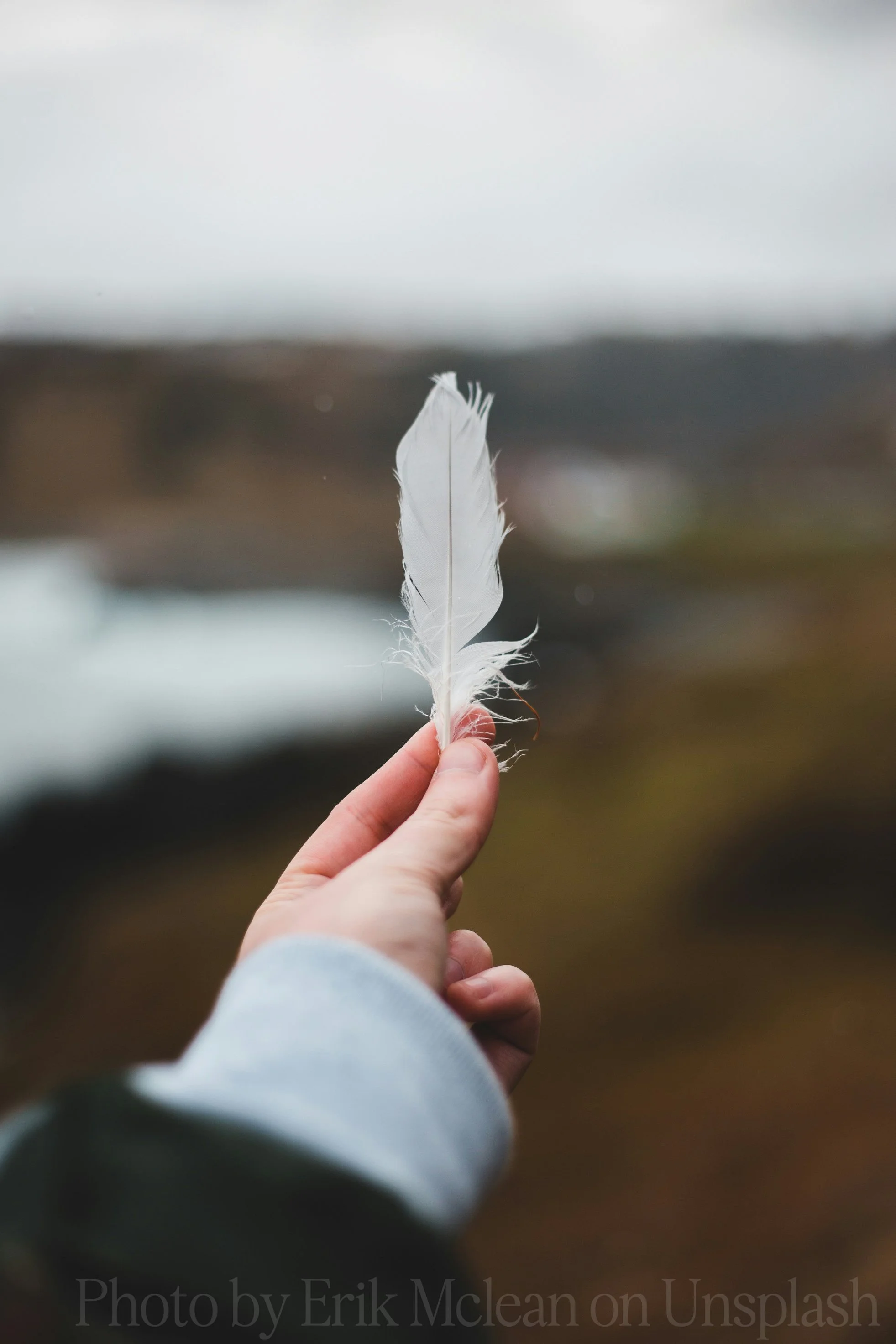 A person holding a white feather outdoors with a blurred background.