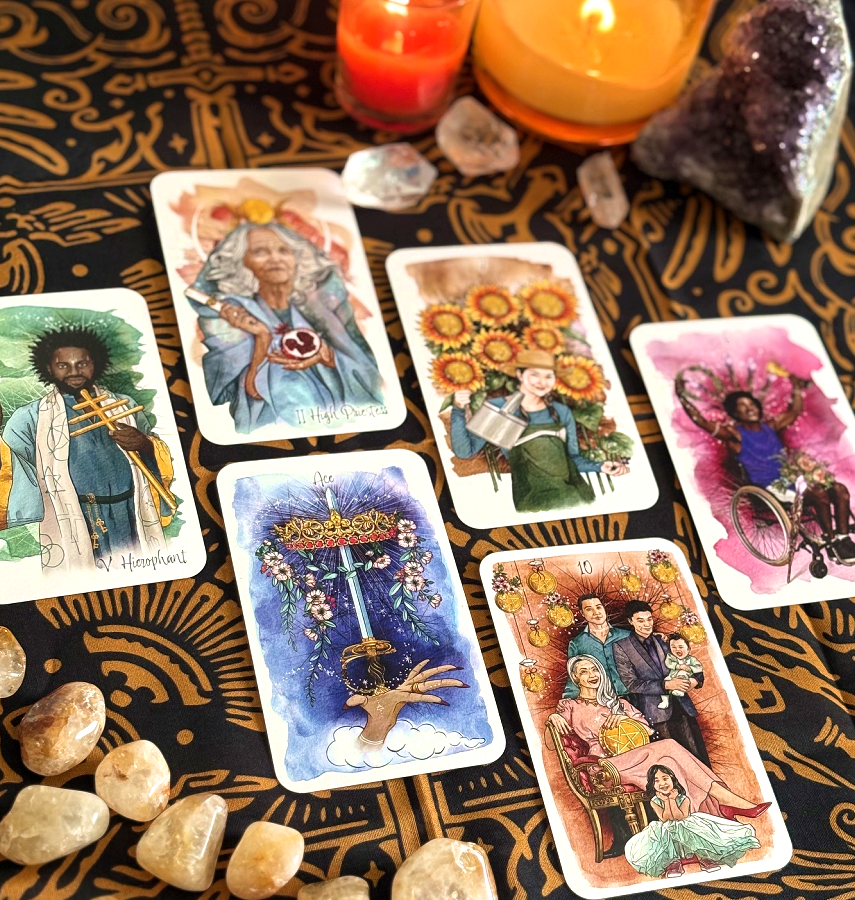 A tarot card reading setup with several colorful tarot cards laid out on a black cloth with gold patterns, surrounded by candles, crystals, and amethyst stones.