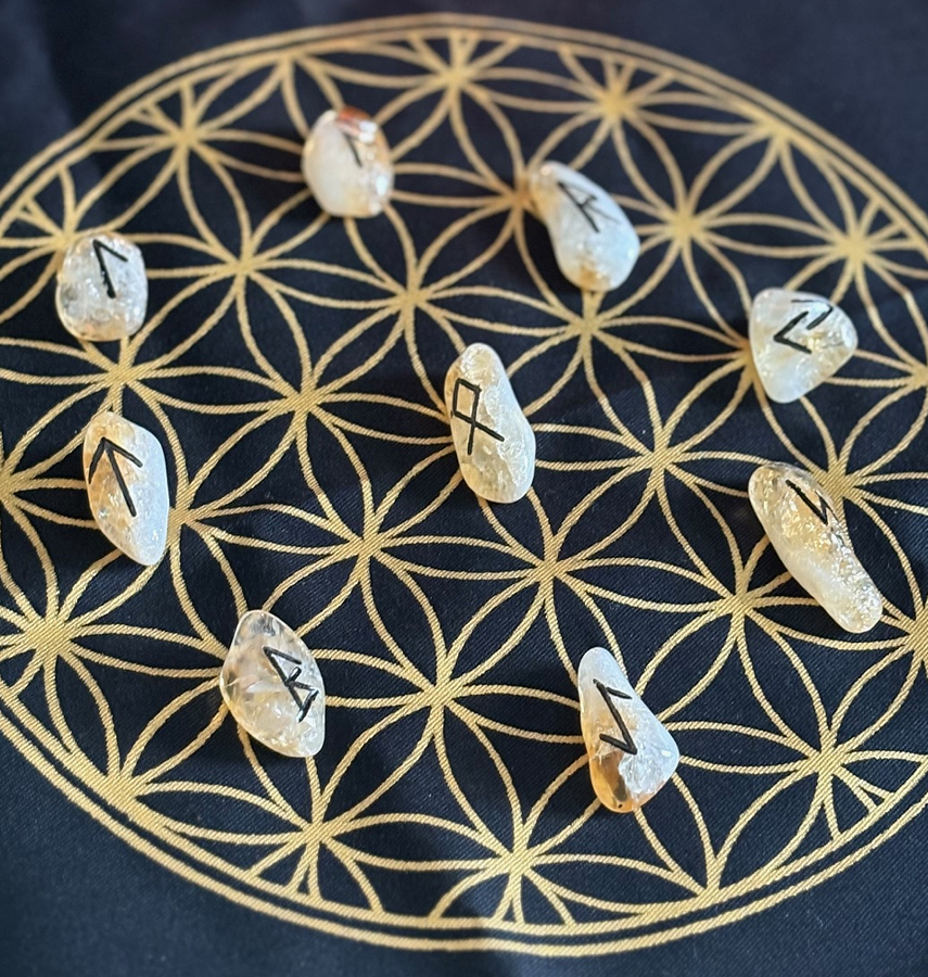 Nine citrine runes are arranged on a black cloth with a gold geometric pattern called the Flower of Life.