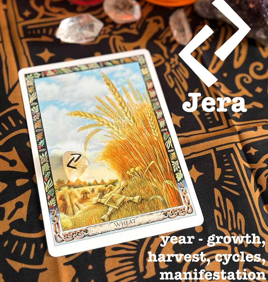 Tarot card labeled 'Wheat' with an illustration of wheat stalks in a field, placed on a patterned cloth. The card has a stone with the rune Jera on it. Informational text explains that Jera means year, growth, cycles, harvest, manifestation