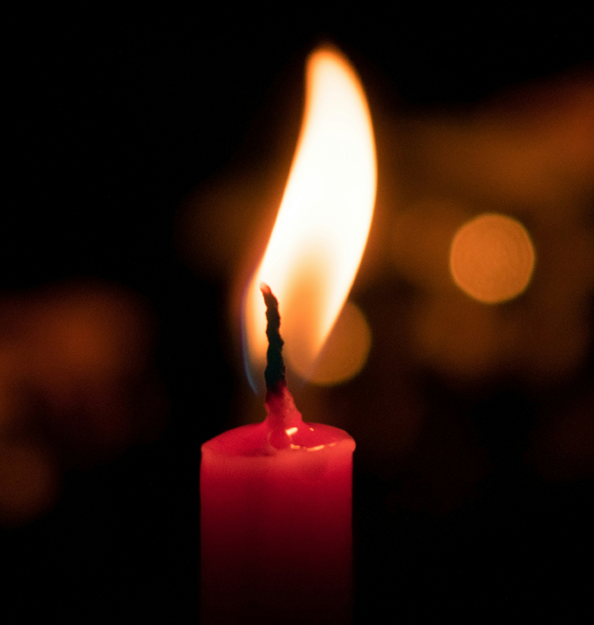 Close-up of a lit red candle with a bright flame against a dark background.