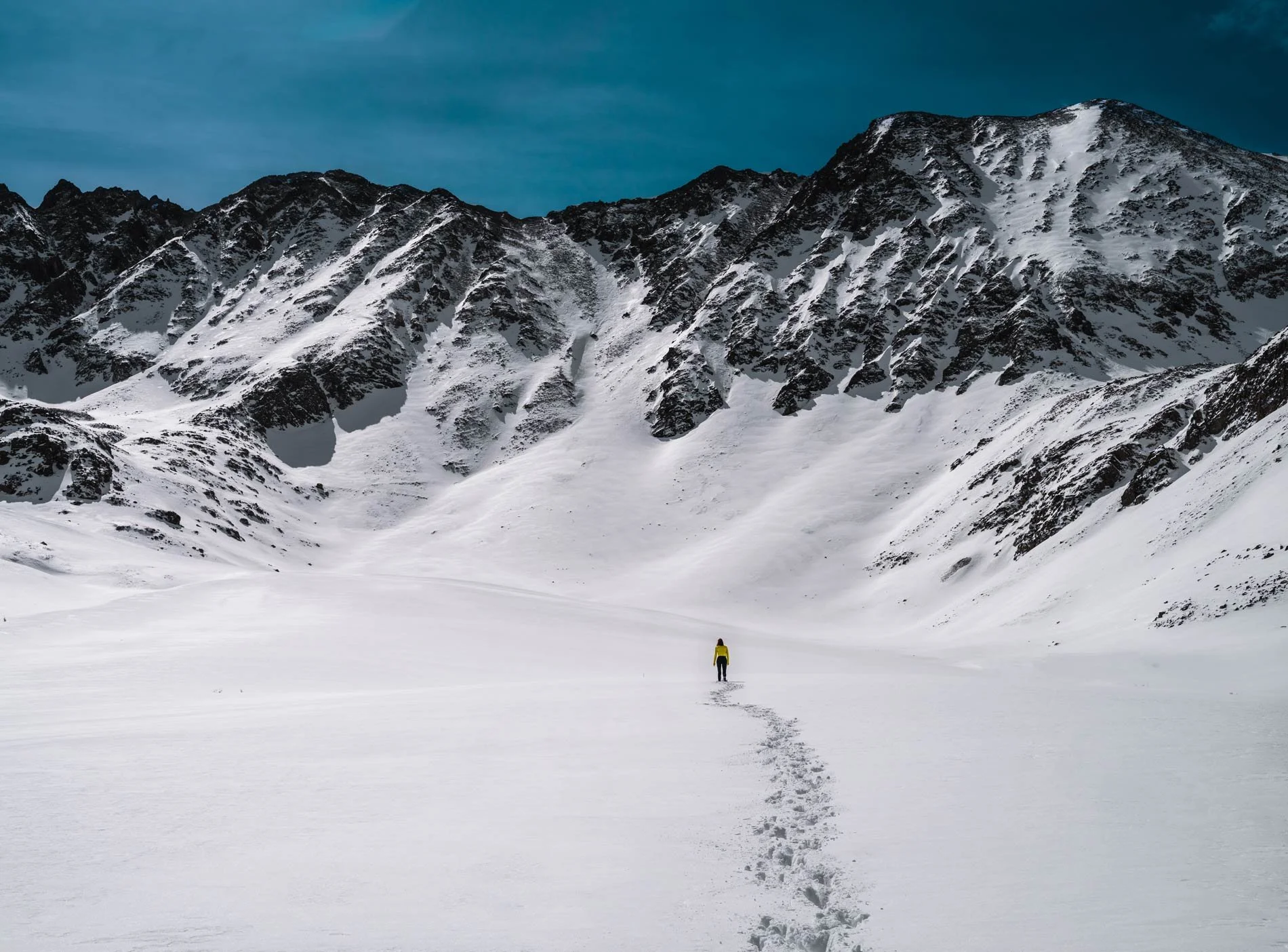 Hiker setting track in the snow, facing a snow-covered mountain