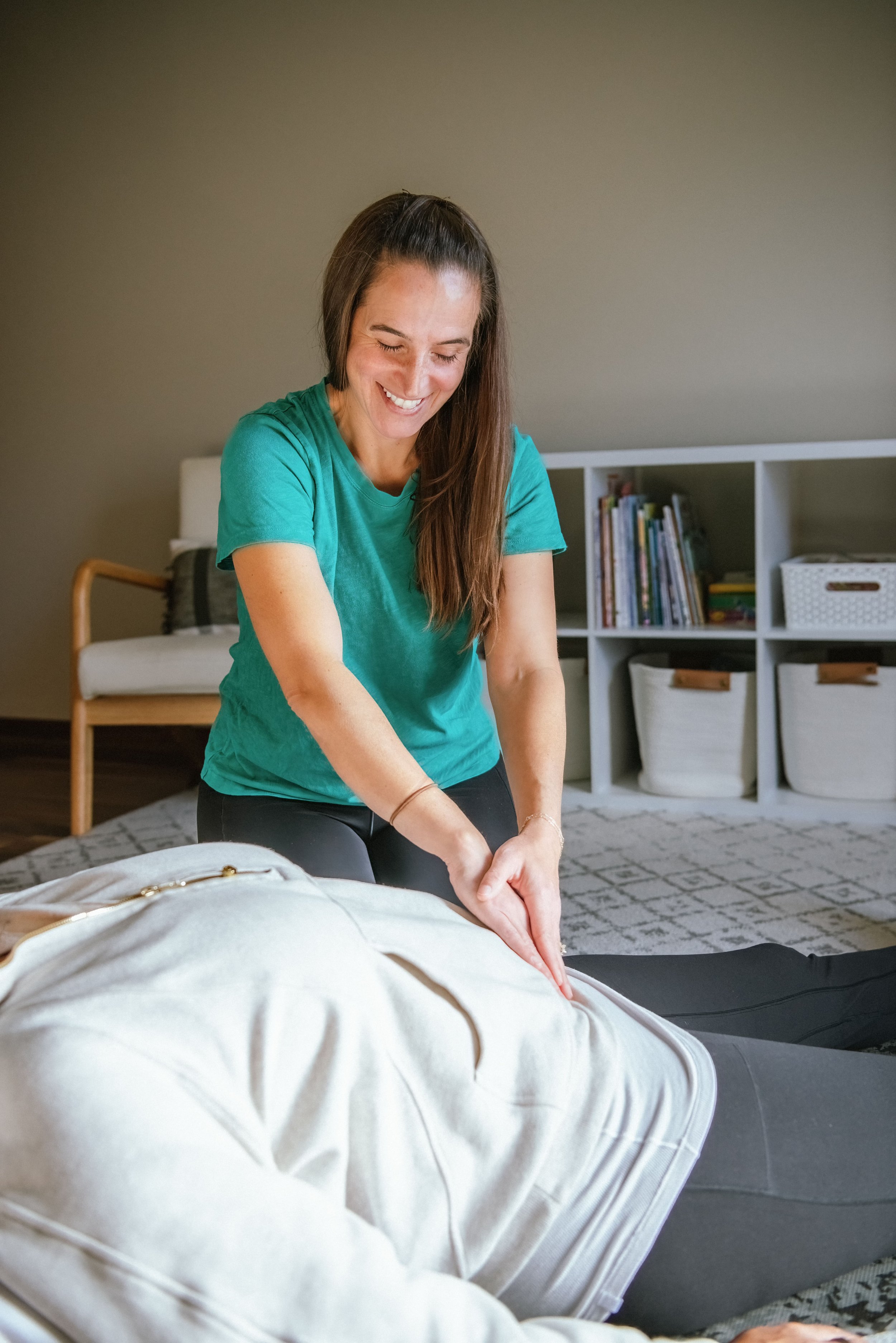 A woman practicing reiki or energy healing on a person laying on the floor in a cozy room with bookshelves.