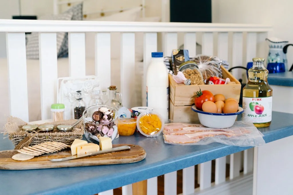 Kitchen counter with breakfast ingredients including cheese, cookies, yogurt, eggs, bacon, apple juice, and various jars and food items.