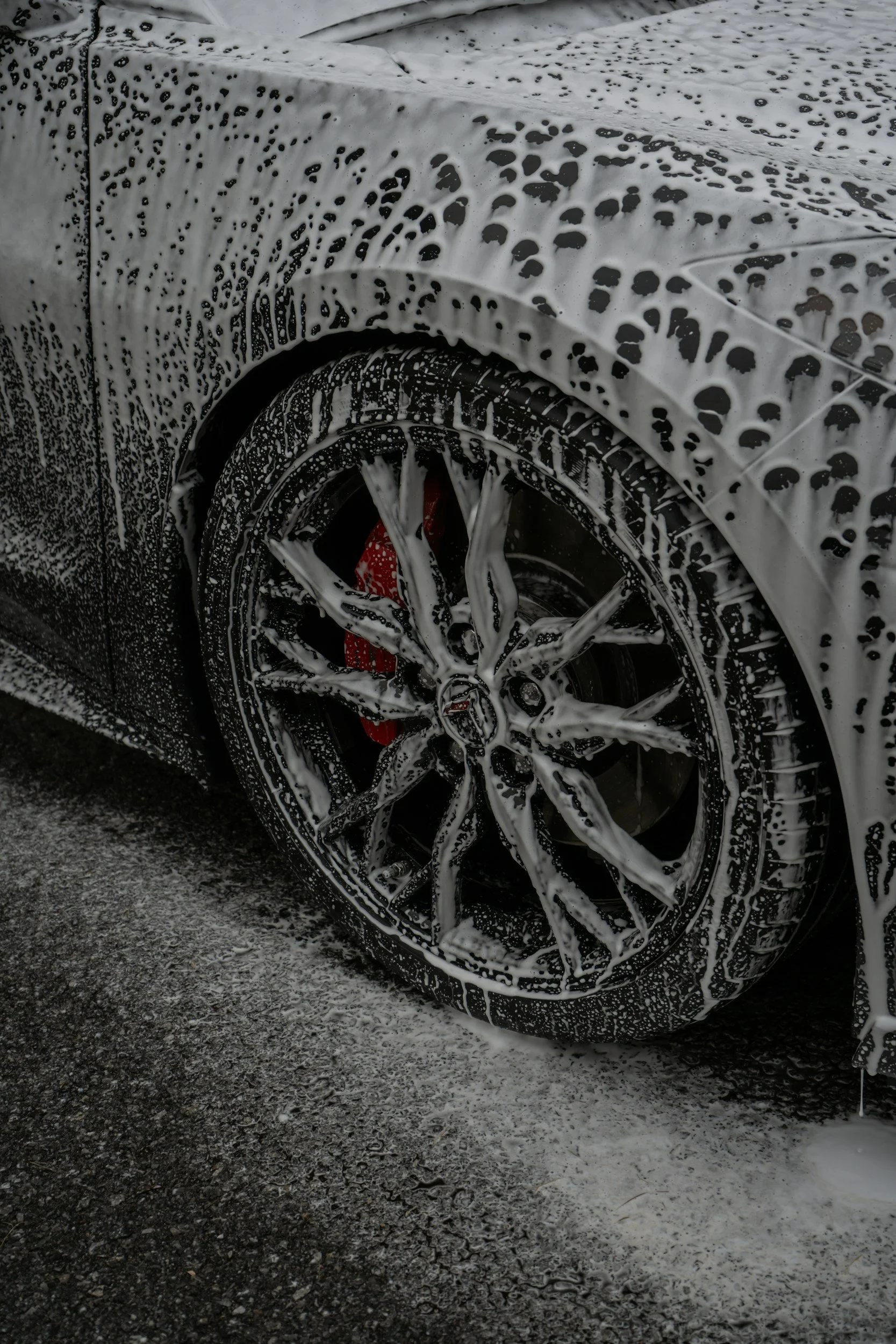 Close-up of a car wheel covered in soap suds during washing, with soap bubbles on the tire and car body.
