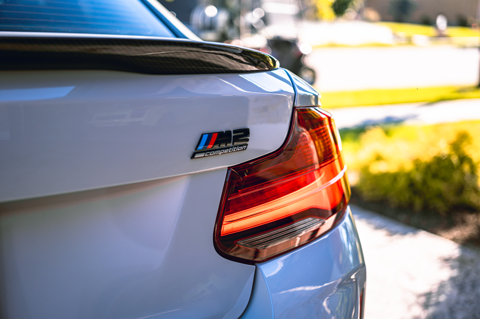Close-up of the rear of a white BMW M2 Competition car, showing the taillight and the M2 badge